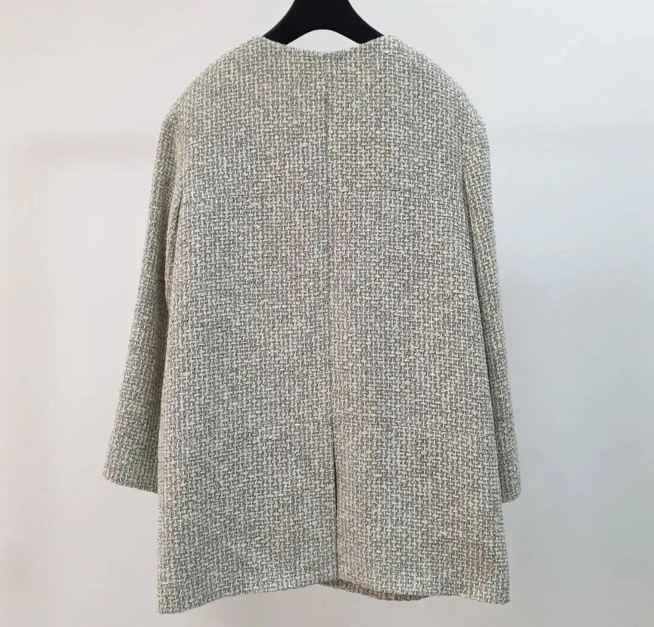 From the Spring 2014 Collection. Creme and grey Chanel tweed short coat with dual welt pockets, structured shoulders, crew neck, chain at interior hem, interlocking CC embellishment at front and hook-and-eye closures at front.

Sz.40

Like new