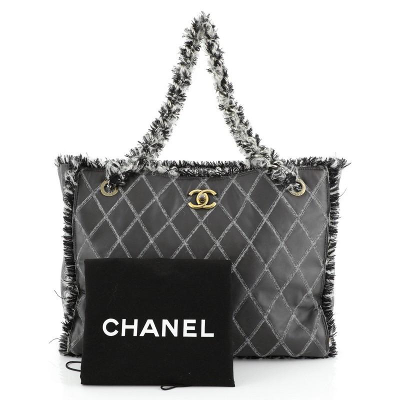 This Chanel Tweedy Tote Quilted Leather Large, crafted from gray quilted leather with tweed, features chain straps wrapped in tweed, black and white tweed fringe trim, protective base studs, and aged gold and aged silver-tone hardware. Its CC