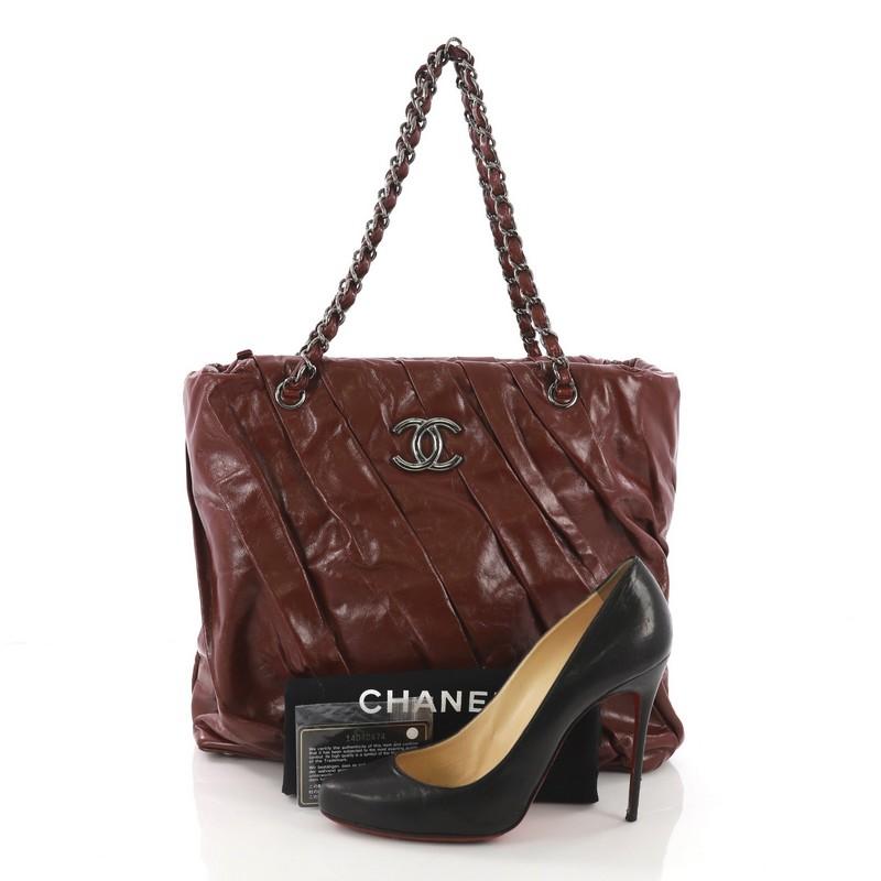 This Chanel Twisted Tote Glazed Calfskin Medium, created from dark red glazed calfskin, features woven-in leather silver chain straps, CC hardware accents, four base studs, and gunmetal-tone hardware. Its top zip closure opens to a gray satin