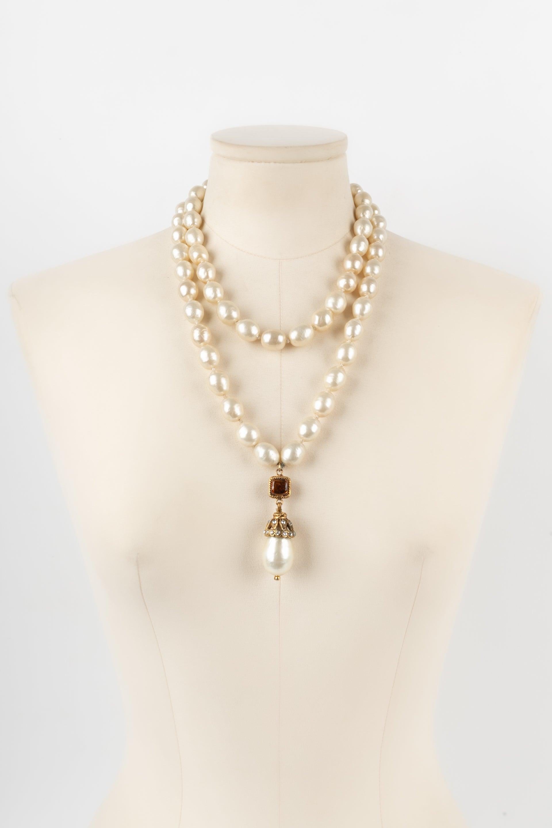 Chanel - (Fabriqué en France) Collier composé de deux rangs de perles fantaisie assemblées par nœuds, d'un pendentif, d'une attache en métal doré, et de pâte de verre. Bijoux des années 1980.

Informations complémentaires :
Condit : Très bon