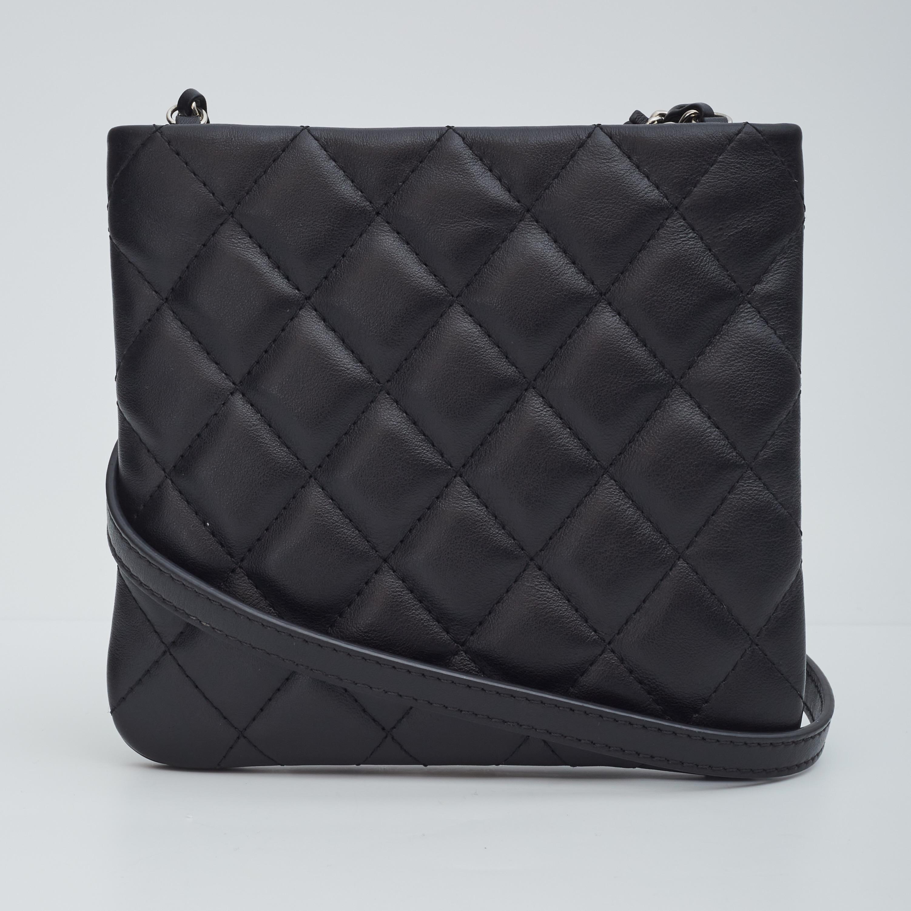 This Chanel crossbody bag made of lambskin leather in black. The bag features a flat design, diamond quilted stitching, a front cc logo, silver hardware and a signature chain and leather shoulder strap. The bag is finished with black woven fabric
