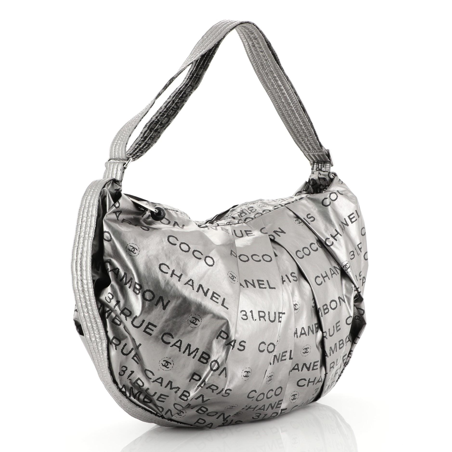 This Chanel Unlimited Shoulder Bag Nylon Large, crafted in silver printed nylon, features an adjustable flat strap, printed Chanel Paris 31 Rue Cambon all over, and silver-tone hardware. Its zip closure opens to a black fabric interior with zip and