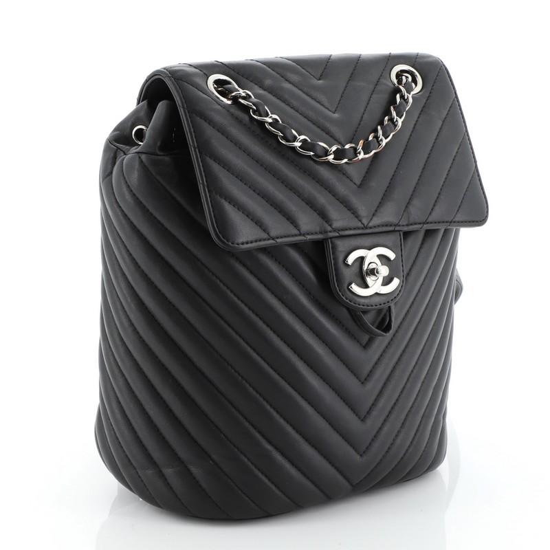 This Chanel Urban Spirit Backpack Chevron Calfskin Small, crafted from black chevron calfskin leather, features adjustable leather shoulder straps, exterior back pocket, and silver-tone hardware. Its cinch cord opening and CC turn-lock closure opens