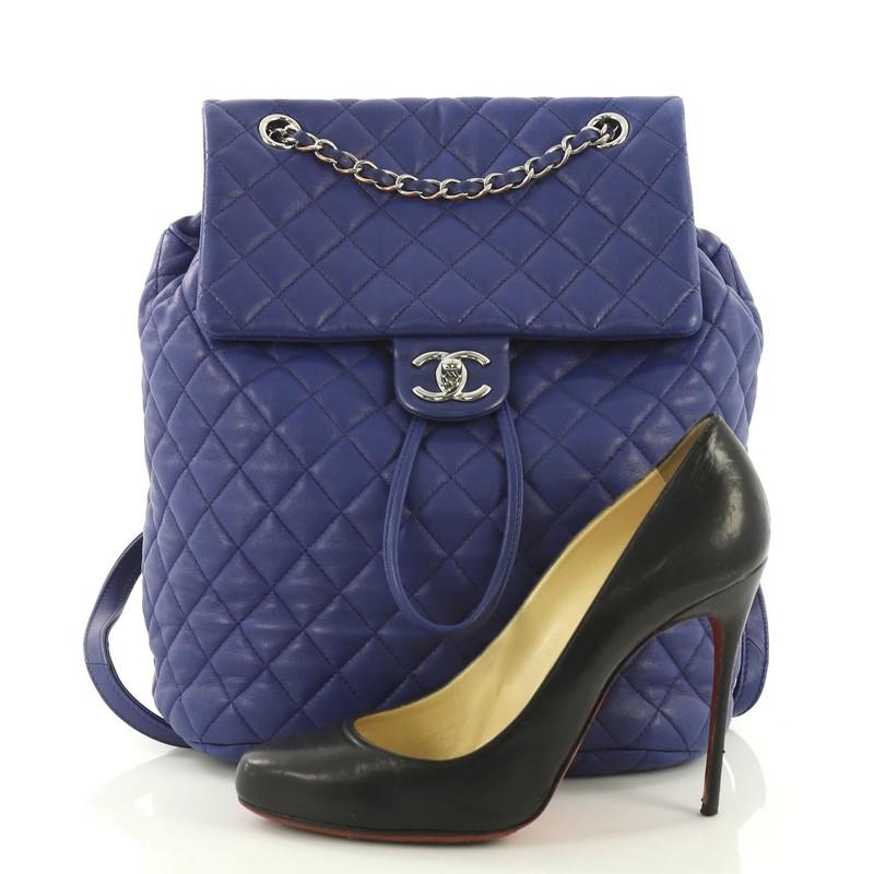 This Chanel Urban Spirit Backpack Quilted Lambskin Large, crafted in blue quilted lambskin, features a frontal flap, woven-in leather chain top handle, flat leather backpack straps, and silver-tone hardware. Its turn-lock and drawstring closure
