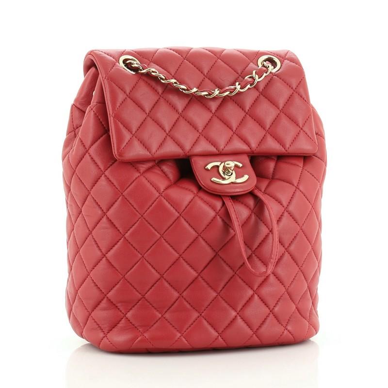 This Chanel Urban Spirit Backpack Quilted Lambskin Small, crafted in red quilted lambskin, features a frontal flap, woven-in leather chain top handle, flat leather backpack straps, and gold-tone hardware. Its turn-lock and drawstring closure opens