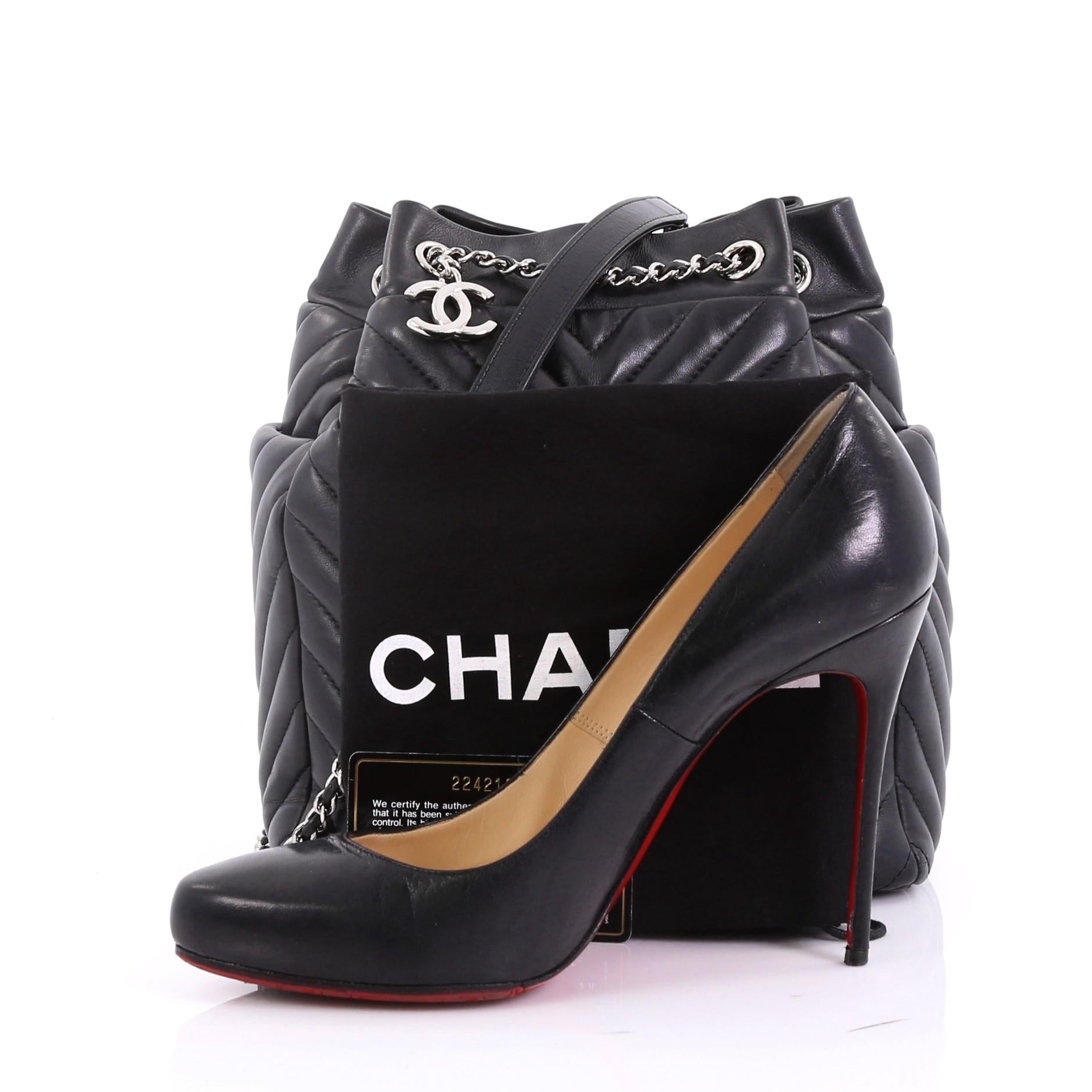 Diese Chanel Urban Spirit Drawstring Bag Chevron Calfskin Small:: gefertigt aus schwarzem Chevron-Kalbsleder:: verfügt über einen eingewebten Lederkettenriemen mit Lederpolsterung:: einen baumelnden CC-Anhänger:: äußere Seitentaschen und