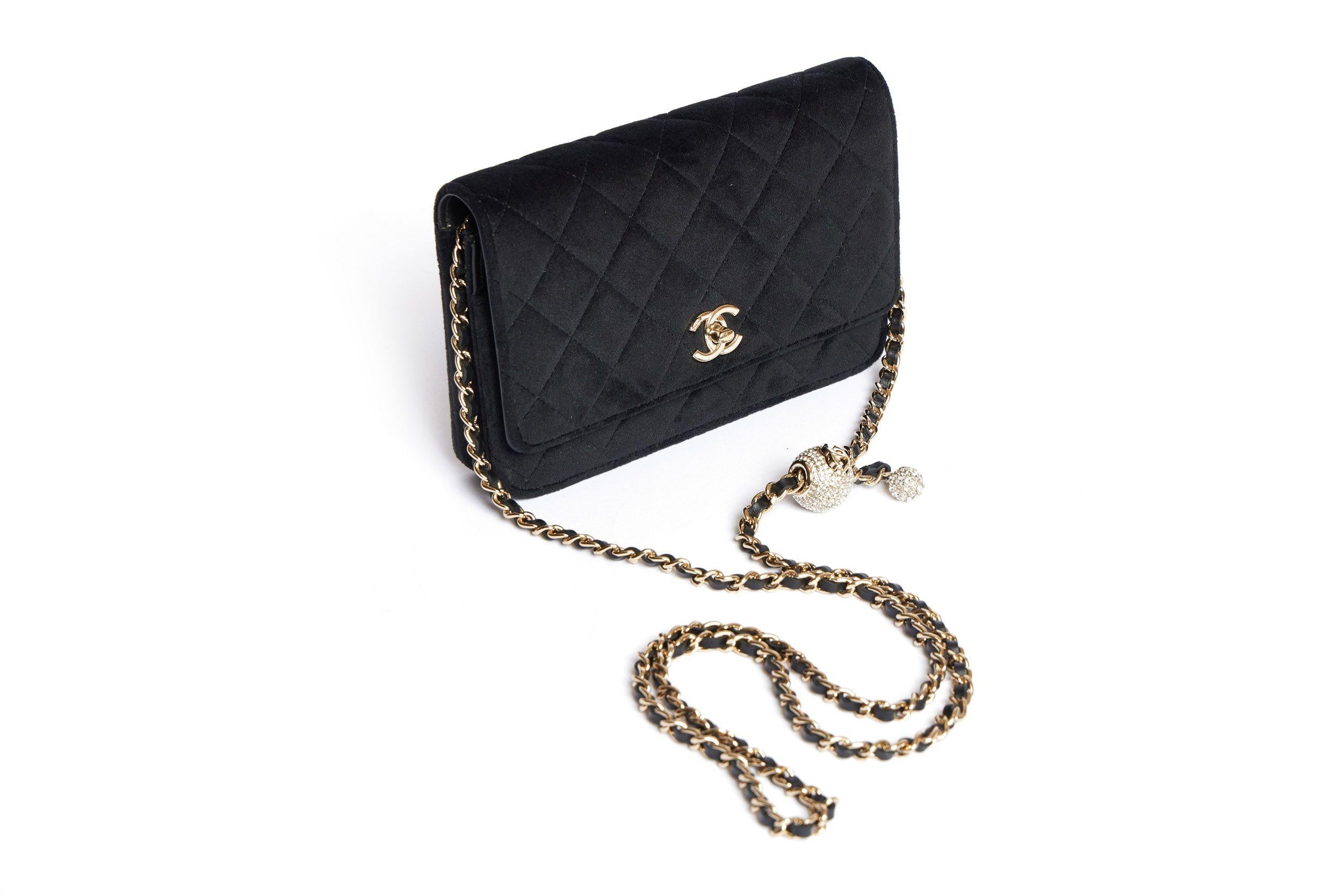 Chanel Velvet wallet on a leather-threated gold chain with a rhinestone charm attached to it. The charm is a ball with a CC logo and one smaller ball hanging on it. The shoulder drop is 23. The bag closes with a CC logo turn lock on the flap. The
