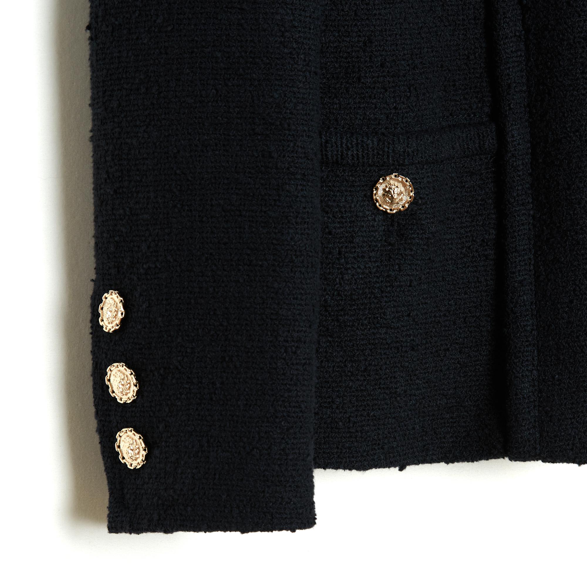 Chanel Uniform straight jacket in black cotton and silk tweed, small collar closed by 5 blackened metal clasps, 4 patch pockets closed by lion head buttons and slightly gold metal (between gold and silver), long sleeves closed by 3 coordinated