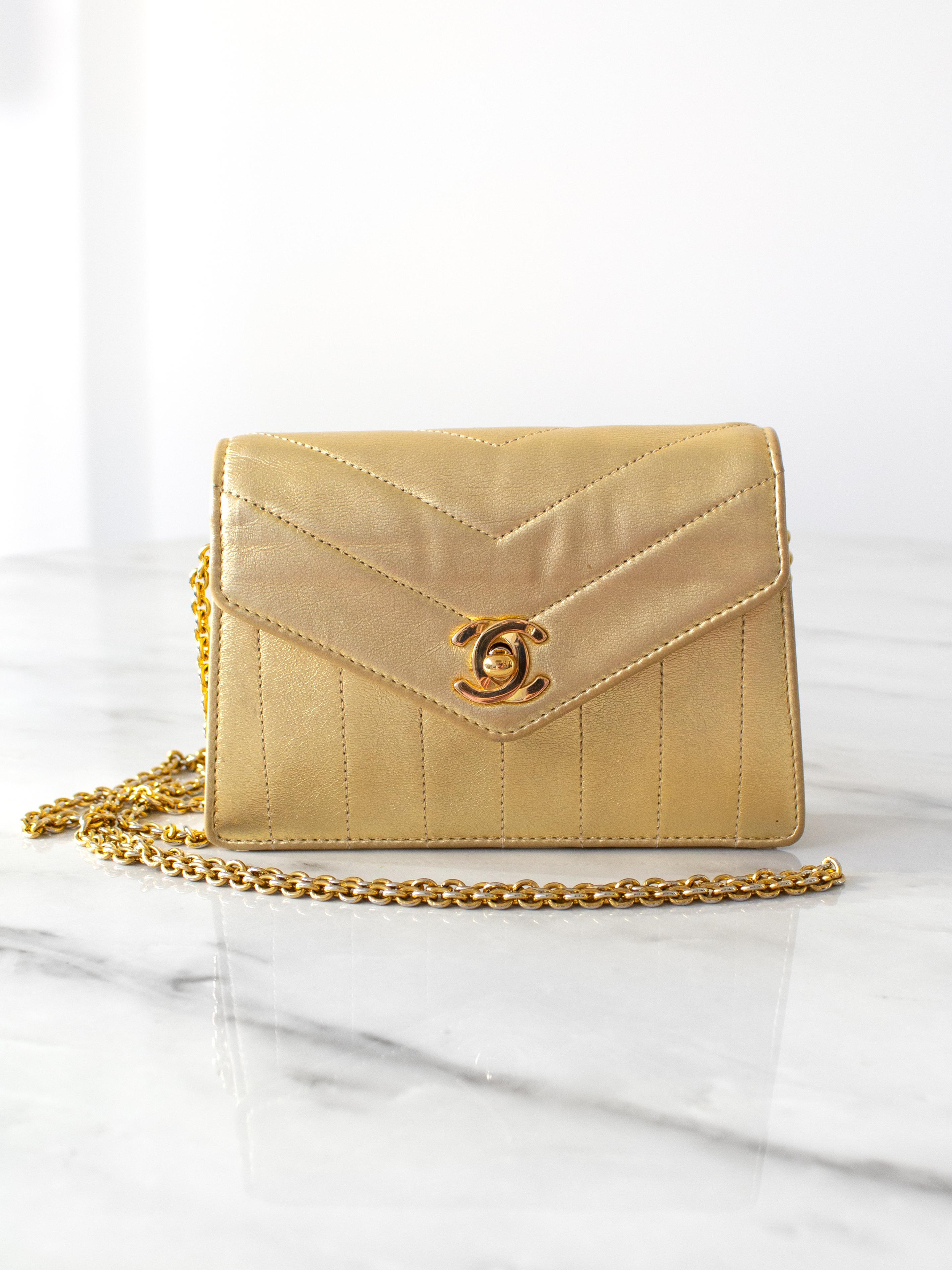 This vintage Chanel mini trapezoid bag from 1980s is a dazzling piece crafted from luxurious lambskin leather in a striking metallic gold hue. It features a 24K gold-plated CC turlock with a hallmark stamp and comes with a long chain strap and an