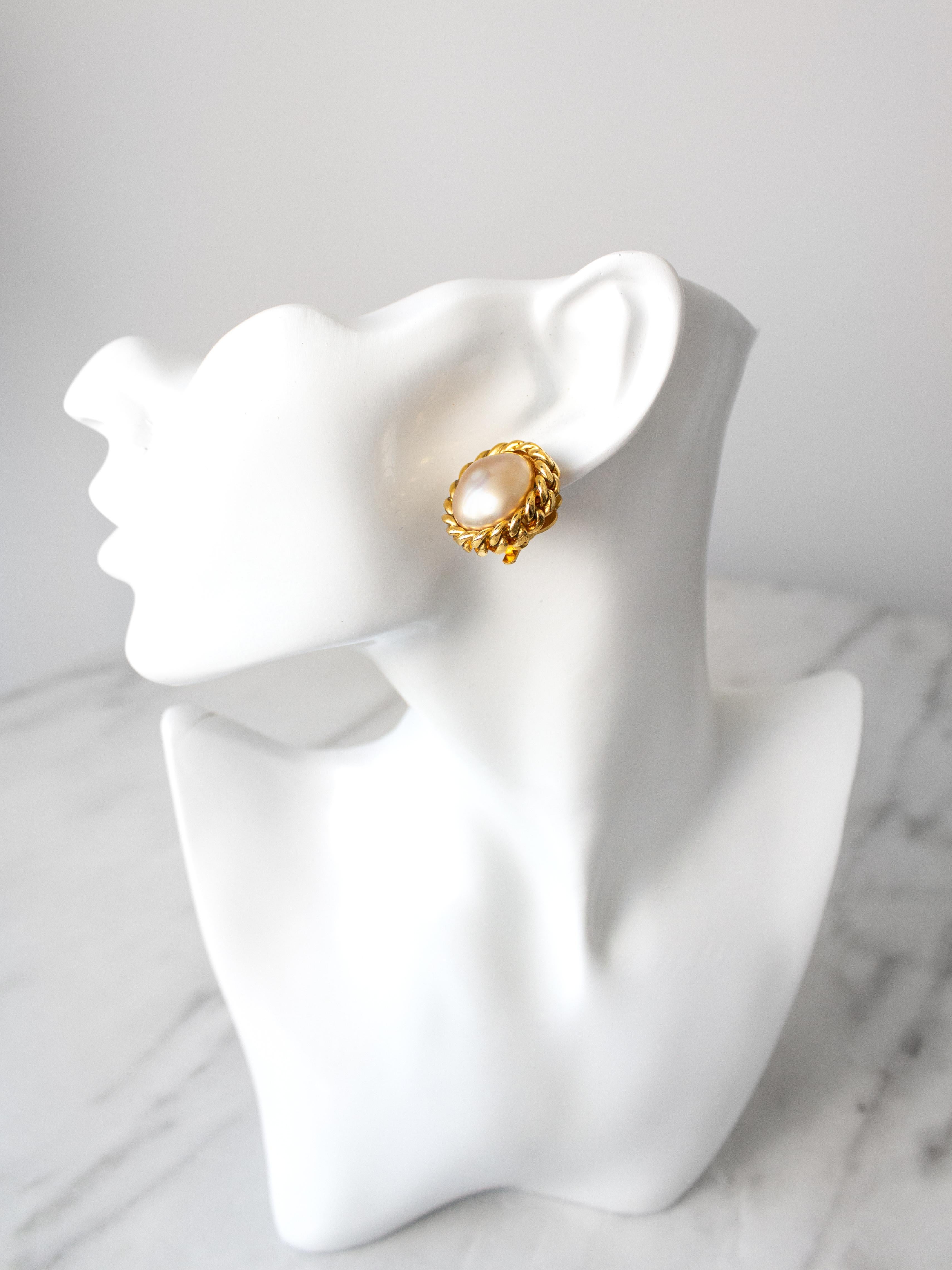 A classic pair of clip-on earrings by Chanel, circa 1980s. They feature a lustrous creamy white faux pearl at their center, delicately encased in gold-plated metal. Chanel's costume jewelry from the 1980s and 1990s remains highly sought after due to