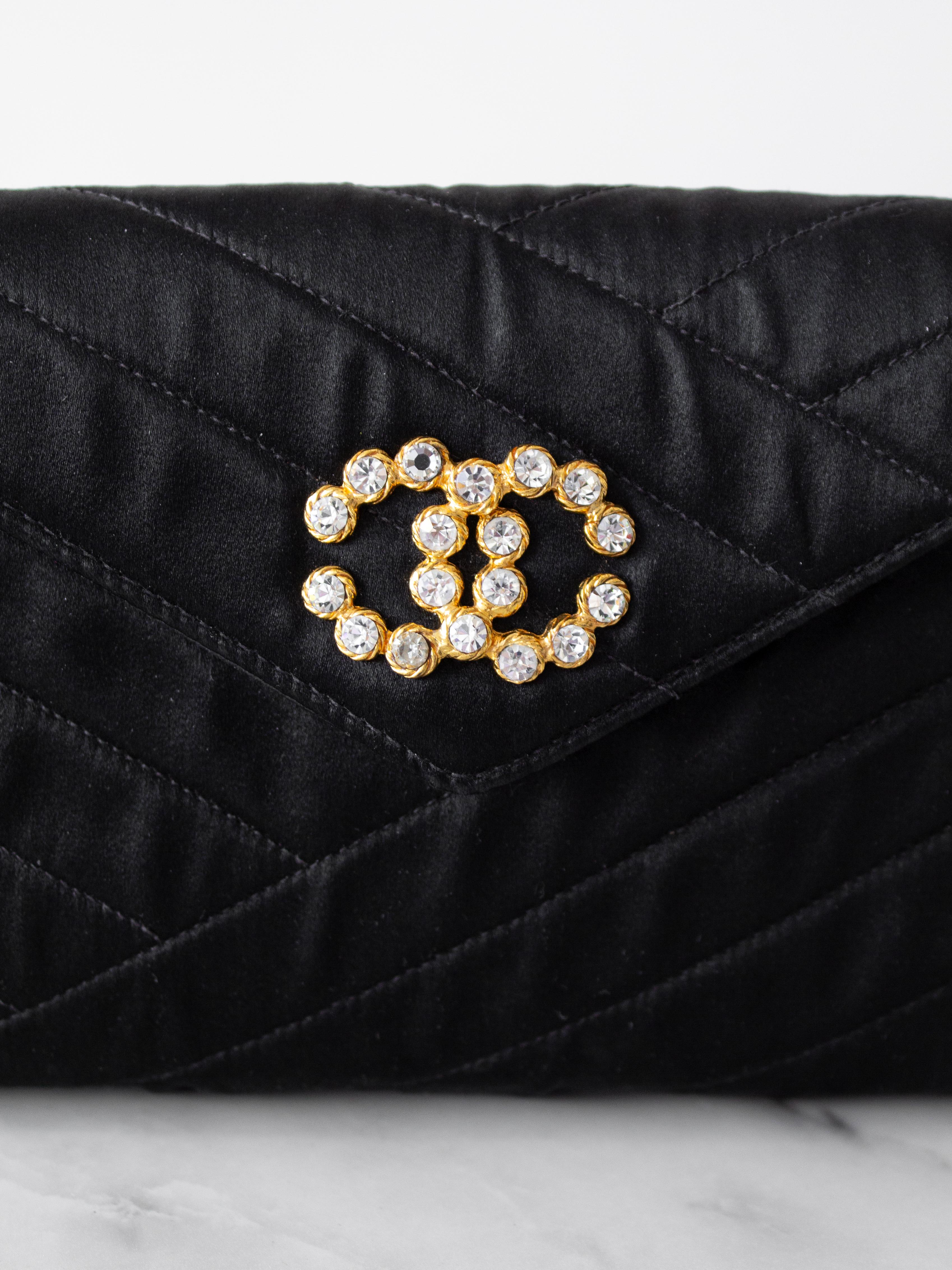 Voici le petit sac de soirée noir de Chanel, une pièce intemporelle datant de 1992. Ce mini sac à rabat est doté d'une bandoulière en maillons de chaîne dorés et est méticuleusement confectionné en satin noir avec un matelassage au point de bias.