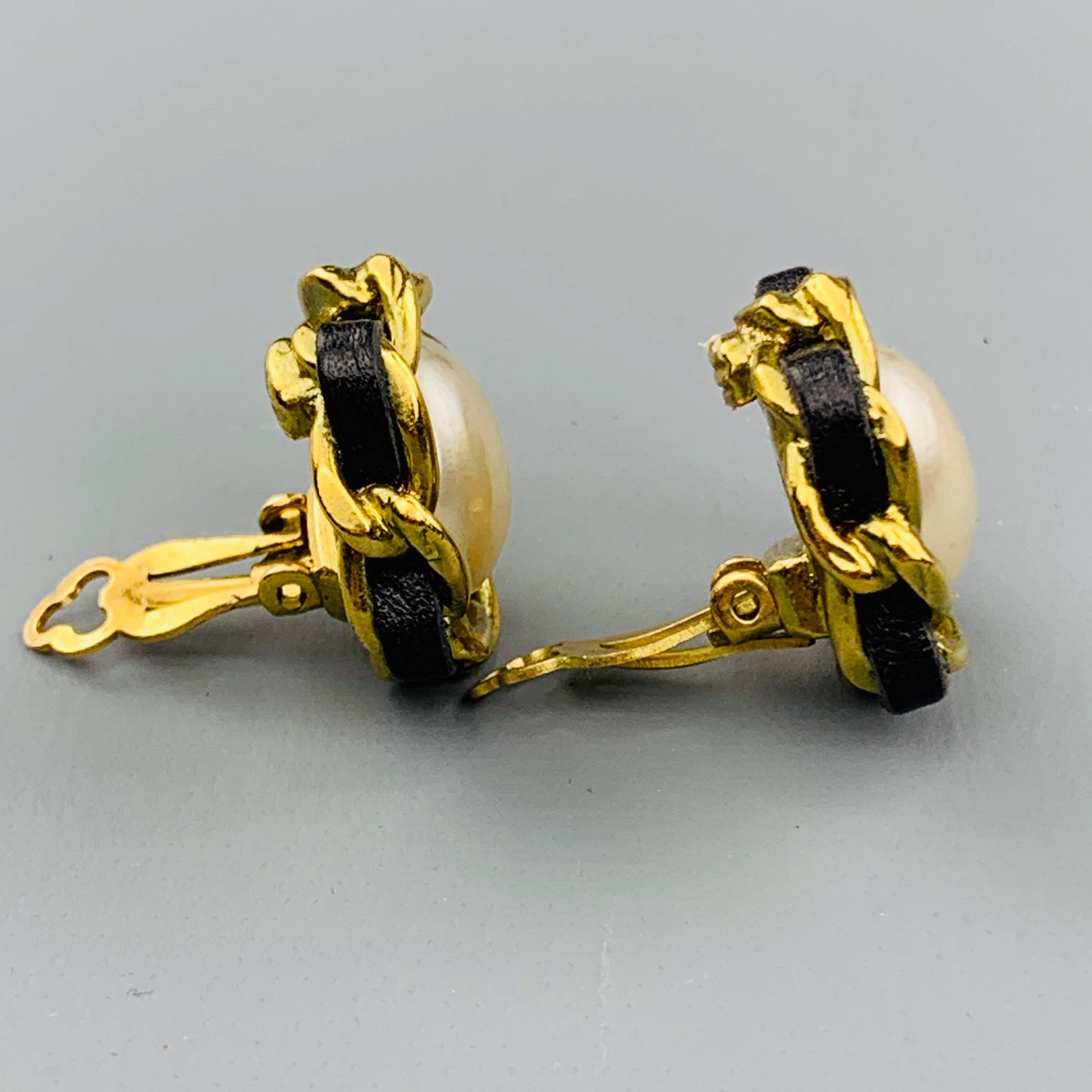 Vintage circa 1994 CHANEL clip on earrings feature a faux pearl encased with gold tone metal chain woven with black leather. Made in France.
 
Good Pre-Owned Condition.
Marked: 94 P
 
2 x 2 cm.