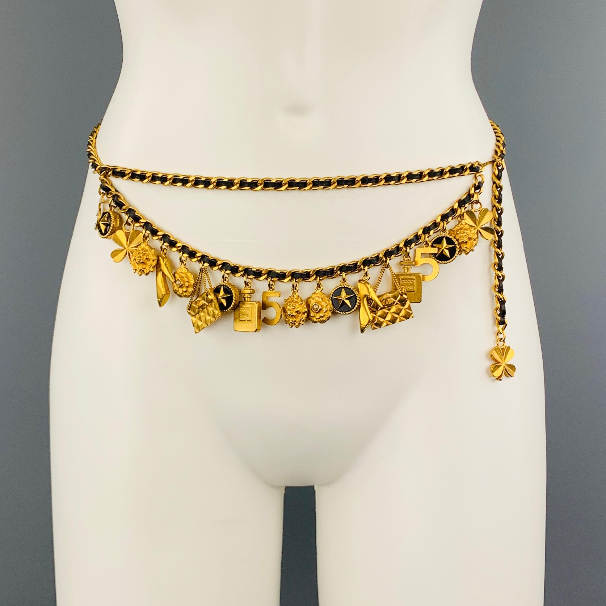 Vintage CHANEL circa 1994 Cruise Collection comes in bold yellow gold tone metal and features a black leather woven chain strap with drop chain adorned with charms in clover, lion's head, star, No. 5, Coco Chanel perfume bottle, purse, camellia