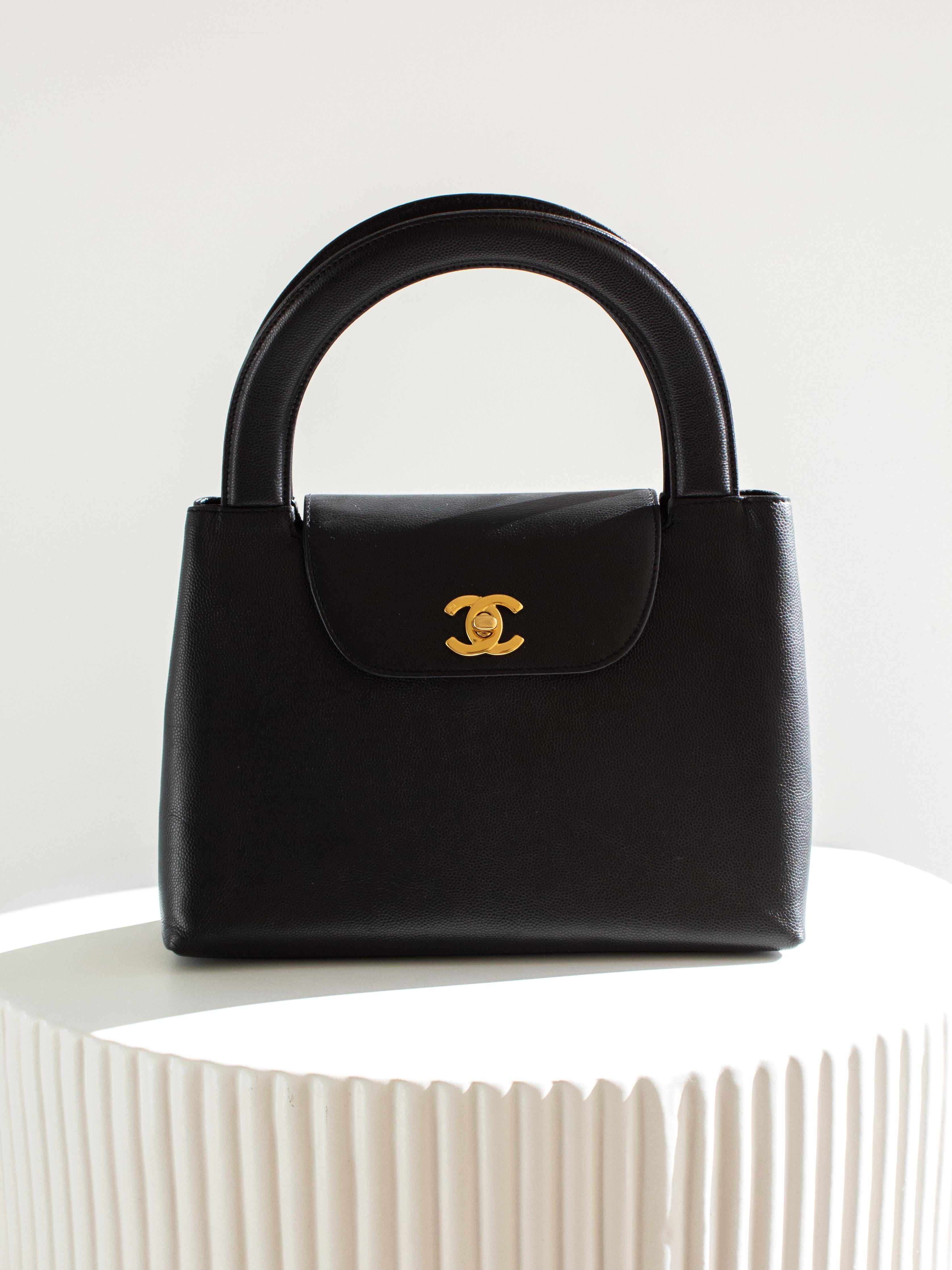 Este bolso de asa superior Chanel Kelly de 1998 es una joya rara en color negro. Fabricado con  de piel de cordero caviar, el bolso está adornado con elegantes herrajes chapados en oro de 24 quilates, incluido el icónico logotipo CC en el cierre.
La