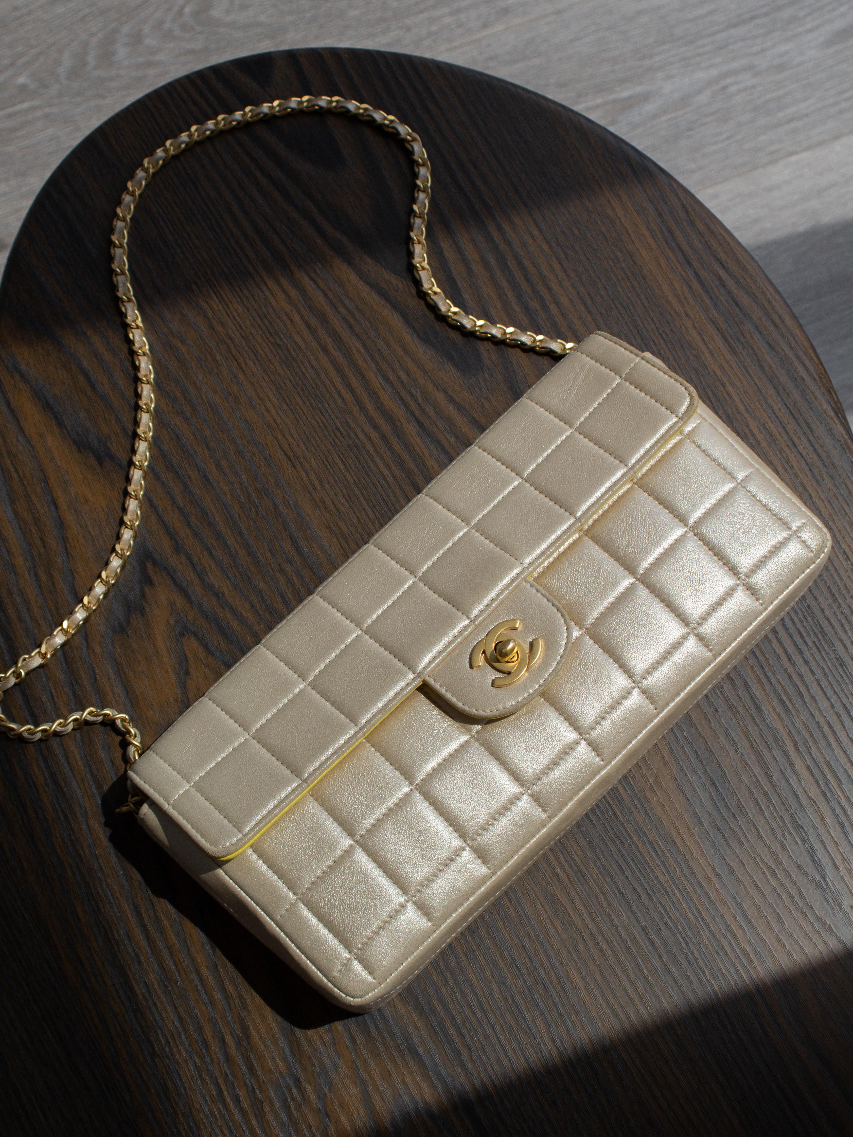 Adoptez les vibrations de l'Icone avec le sac emblématique East West de Chanel datant de 2002. Ce bijou à l'allure rétro affiche une silhouette baguette très tendance et le matelassage caractéristique des barres de chocolat. Confectionné dans un