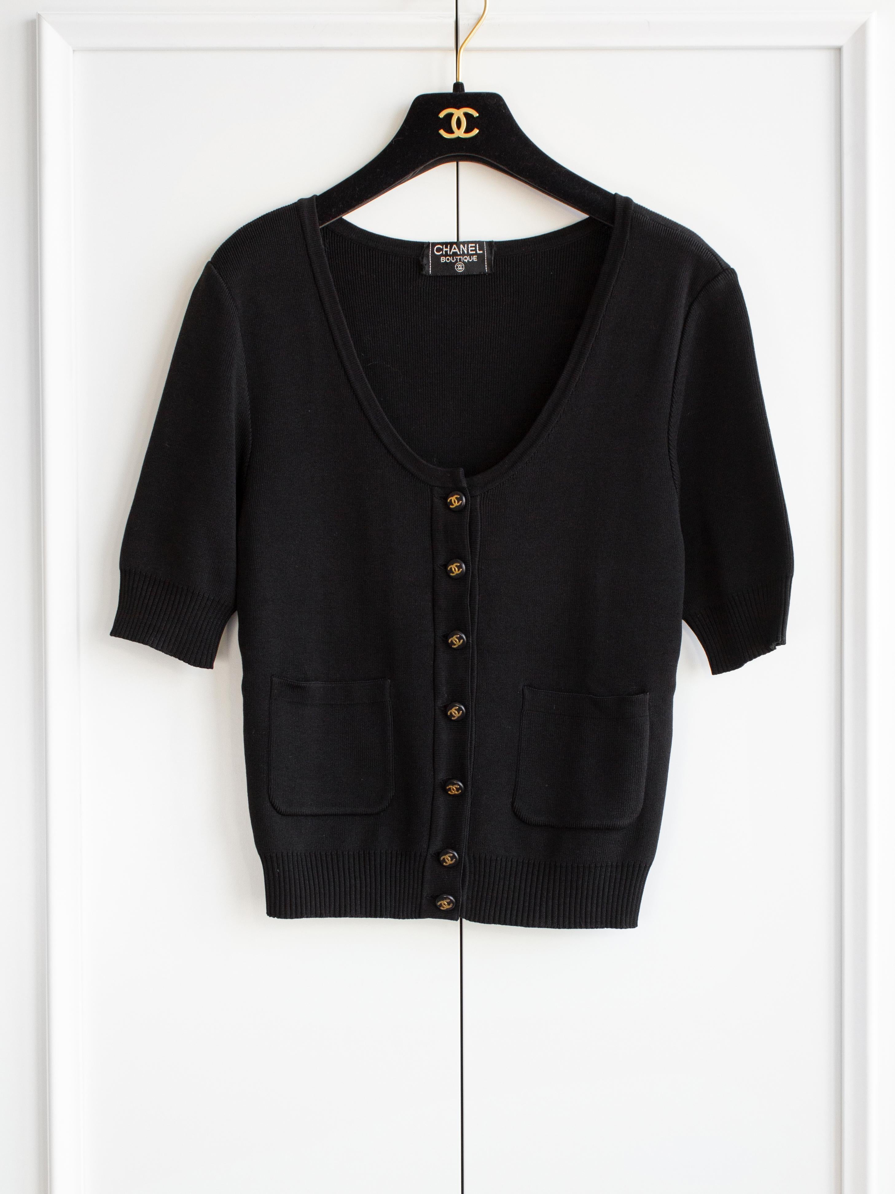 Presenting a classic black knit Chanel cardigan from the mid-90s. This elegant piece features a flattering scoop neck and short sleeves, providing a stylish and comfortable fit. It includes two front pockets for added convenience and is adorned with