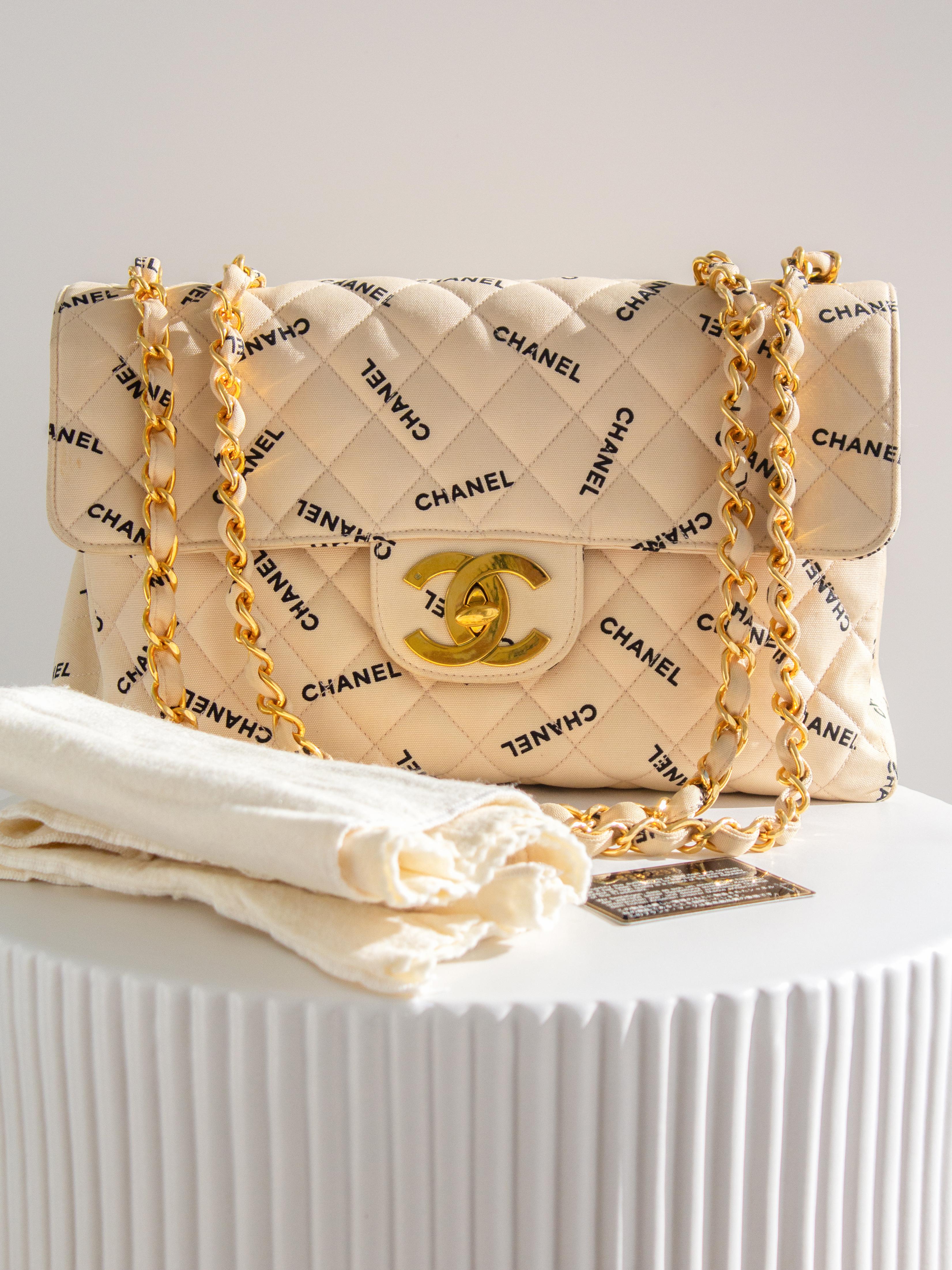 The most wanted beige canvas jumbo XL bag by Chanel! Circa 1994–1996. This stunning, trendy oversized bag is crafted from quilted beige canvas with a contrasting black CHANEL logo throughout, featuring a 24K gold-plated CC turnlock and lambskin