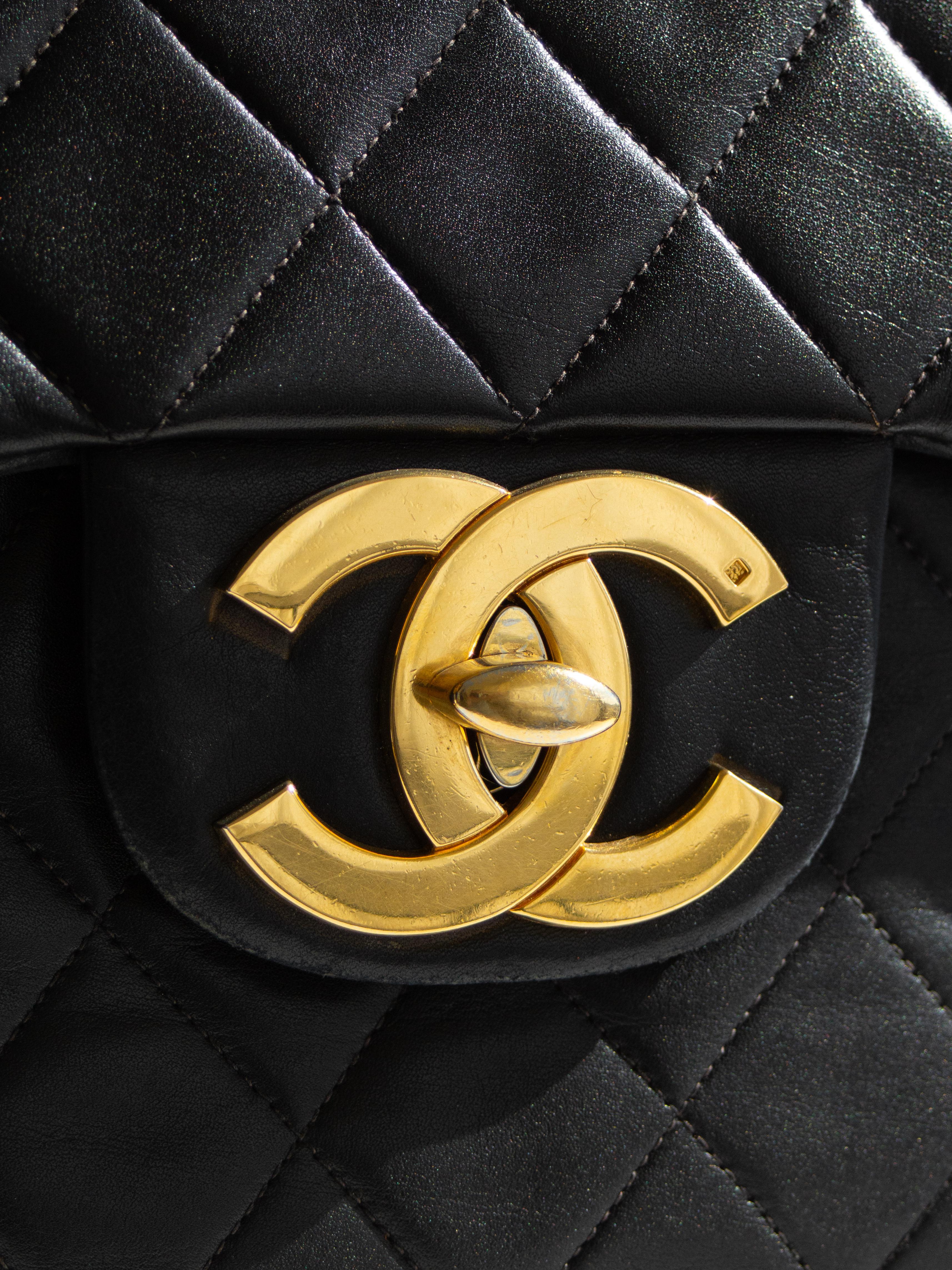 This exquisite Chanel  Jumbo XL flap bag is crafted from quilted black lambskin leather, offering a timeless and elegant appeal. It features a gold chain-link shoulder strap interwoven with black leather, a front flap, and an oversized 24K