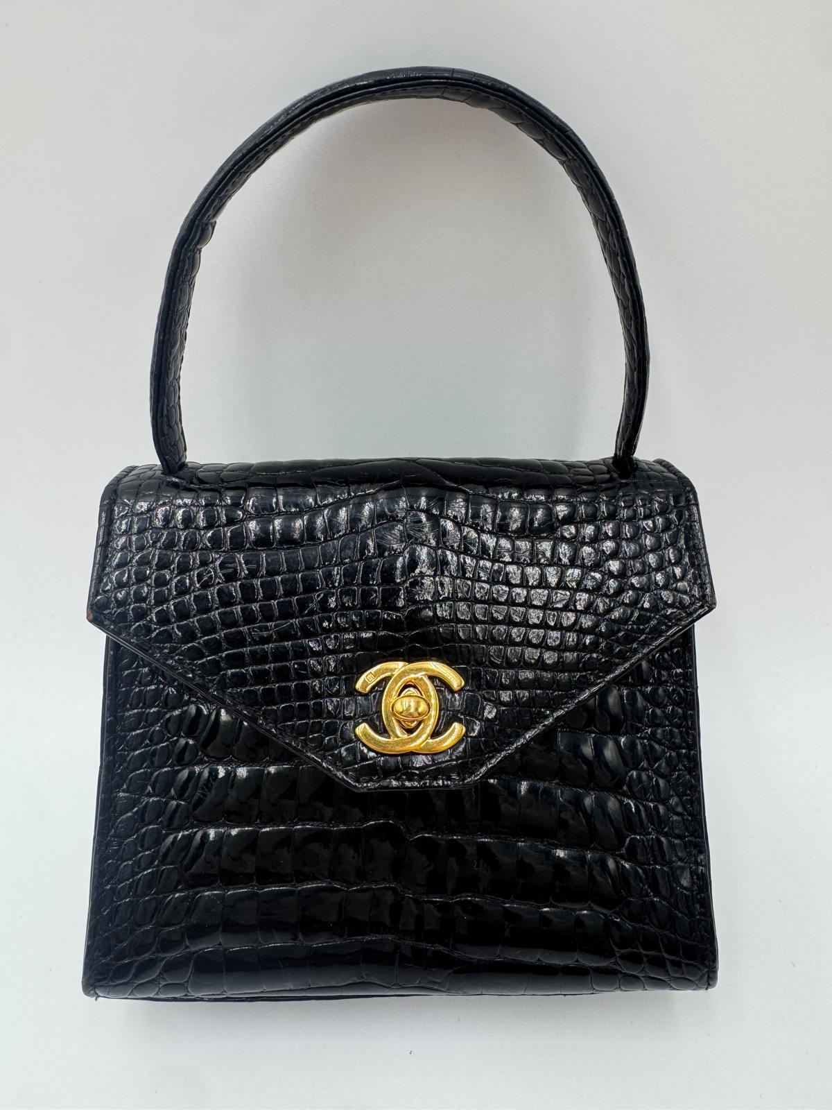 This is a vintage Chanel top handle bag in black crocodile leather with gold-tone hardware and the classic CC turn-lock closure. It features a structured silhouette and a single top handle, making it a standout collector’s piece.

Dimensions: