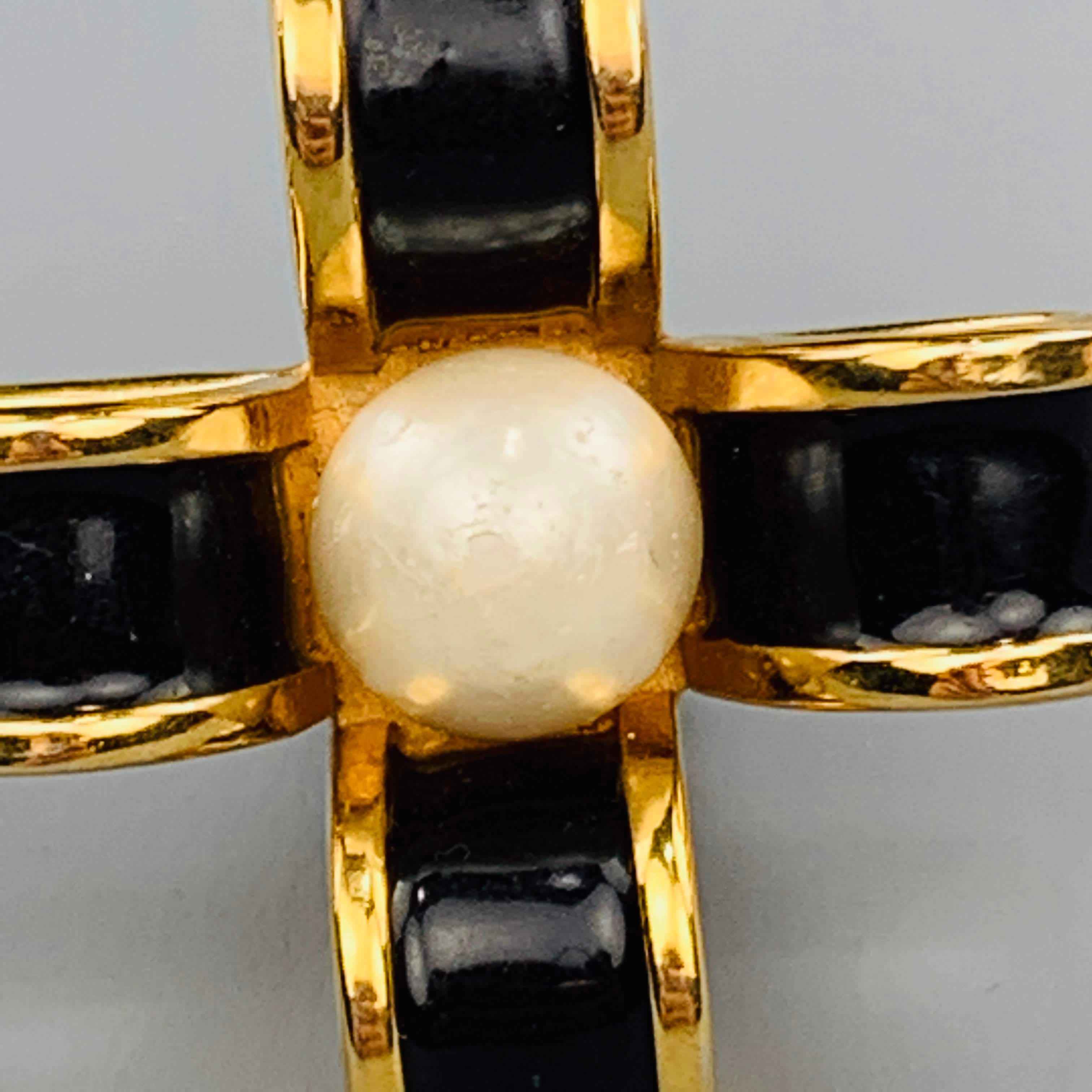 Vintage CHANEL (circa 1954-1971) clip on earrings come in yellow gold tone metal with black enamel in a bow cross motif with a faux pearl center. Wear with age.
 
Good Pre-Owned Condition.
 
4 x 4 cm.