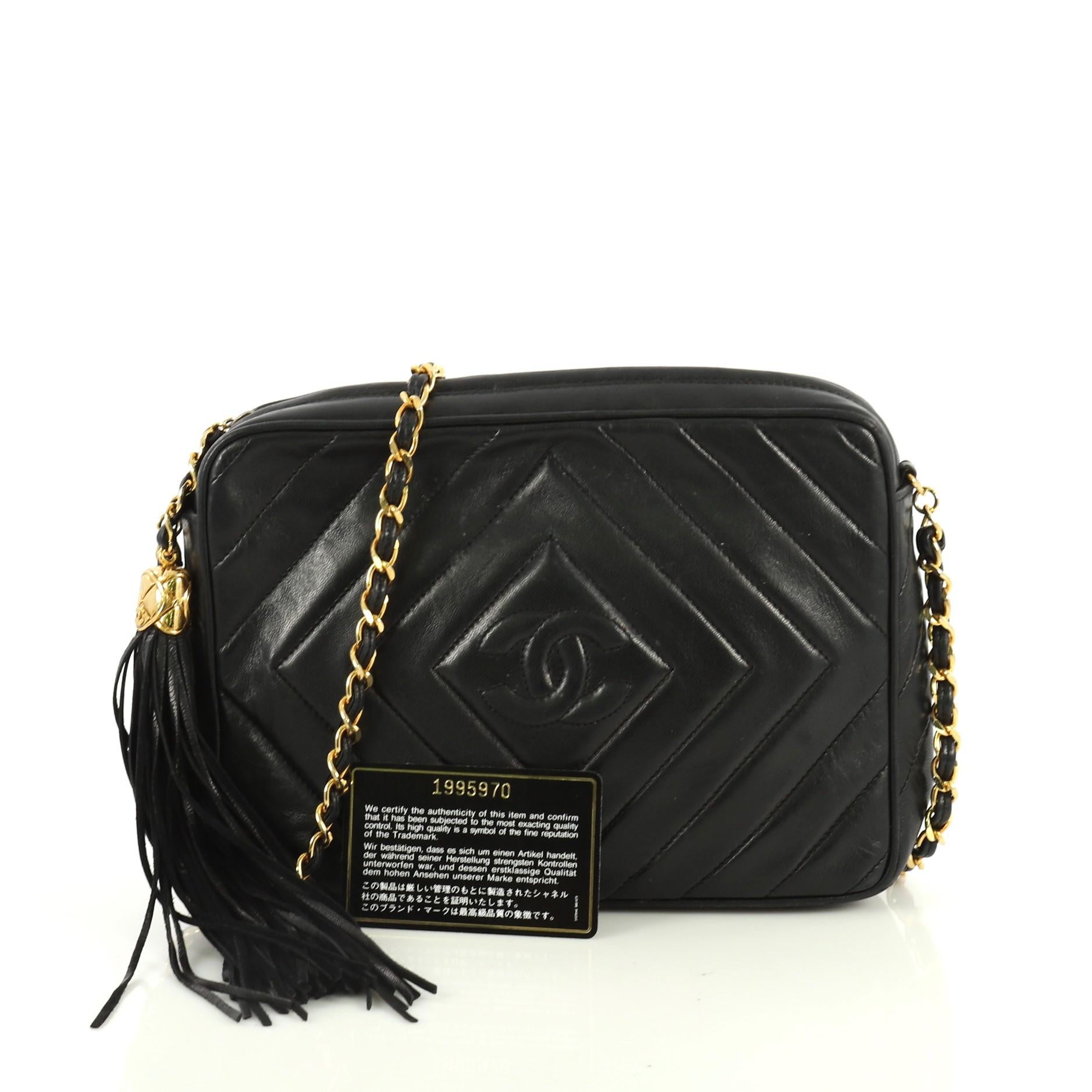 This Chanel Vintage Camera Tassel Bag Chevron Lambskin Small, crafted from black chevron lambskin leather, features woven-in leather chain link strap, leather tassel zipper pull, and gold-tone hardware. Its zip closure opens to a black leather