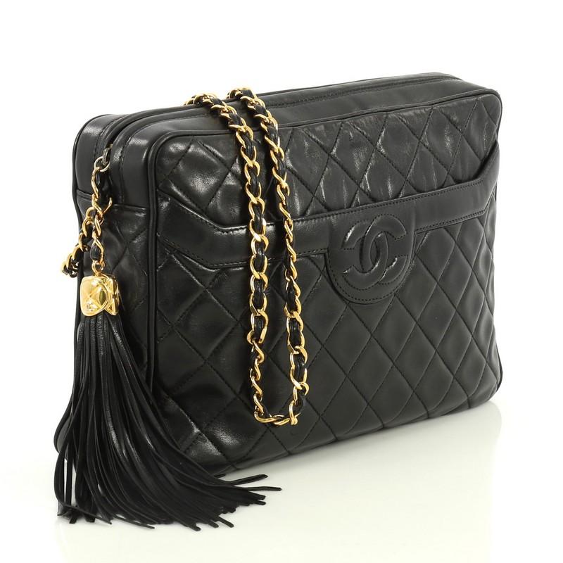 This Chanel Vintage Camera Tassel Bag Quilted Leather Large, crafted in black quilted leather, features woven-in leather chain straps, side tassels with engraved CC charm, and gold-tone hardware. Its zip closure opens to a black leather interior