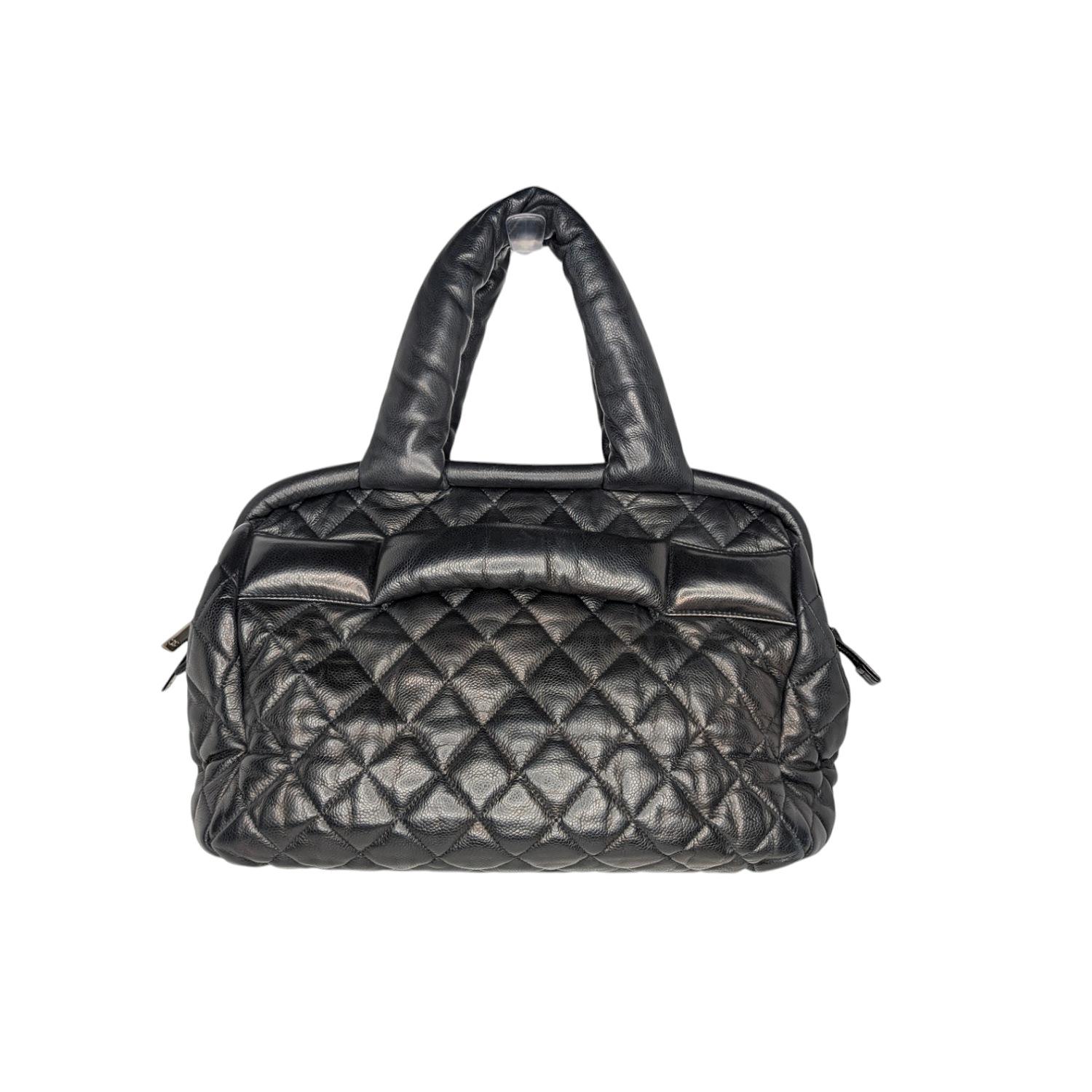 The Chanel Black Caviar Leather Coco Cocoon Bowler Bag is a highly sought after piece from Lagerfeld's fun and chic Coco Cocoon line. This adorable bag was first modeled by British pop star Lily Allen in Chanel's Coco Cocoon ad campaigns and