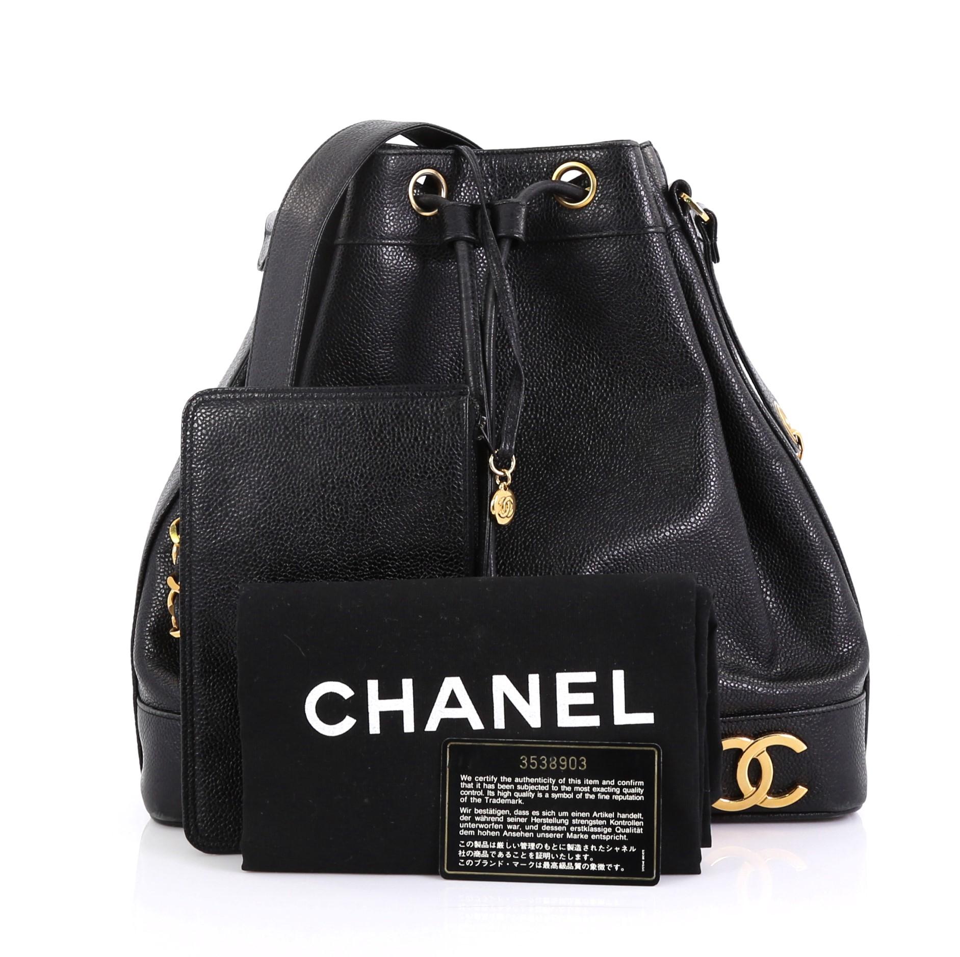 This Chanel Vintage CC Drawstring Bucket Bag Caviar Medium, crafted in black caviar leather, features long woven-in leather chain link strap with leather pad, metal Chanel CC logos at the base, and gold-tone hardware. Its drawstring closure opens to