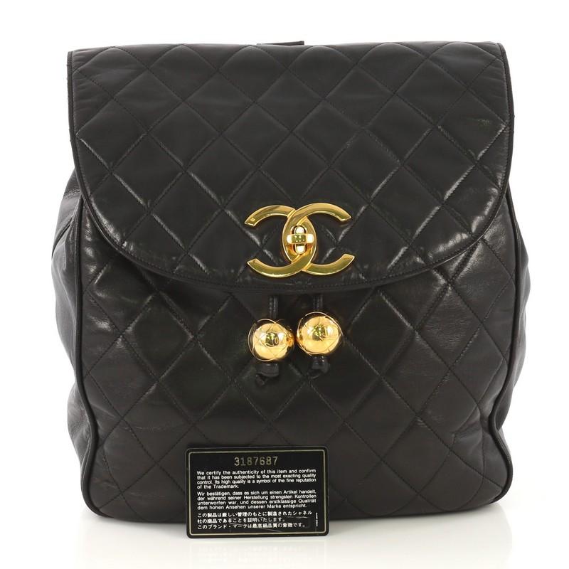 This Chanel Vintage CC Flap Backpack Quilted Lambskin Medium, crafted in black quilted lambskin leather, features dual leather straps and gold-tone hardware. Its CC turn-lock and drawstring closures open to a black leather interior with zip pockets.