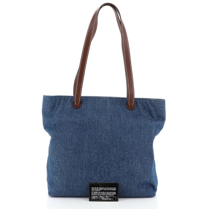 This Chanel Vintage CC Logo Tote Denim Medium, crafted in blue denim, features dual-flat leather handles, stitched CC logo, and matte gold-tone hardware. It opens to a brown fabric-lined interior with side zip pocket. Hologram sticker reads: