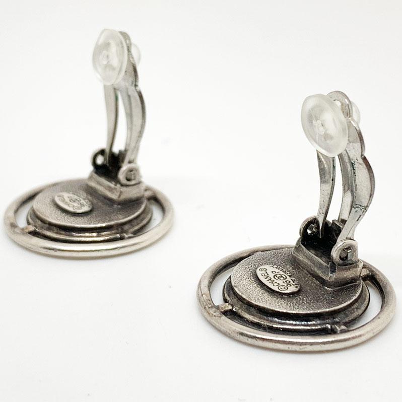 The clips are from Maison CHANEL. They are round, and two-tone silver and gold. They each represent a coin with an effigy character, which is surrounded by the inscription 