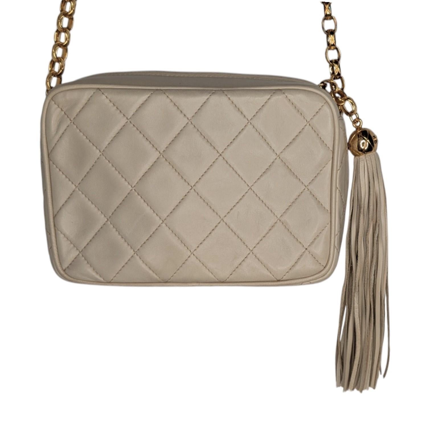 This vintage Chanel camera bag, designed by Karl Lagerfeld in the 90s, exudes timeless elegance. Crafted from cream quilted lambskin, it features 24K gold-tone hardware, the iconic CC logo, and tassel accents. The front pocket and interior zip