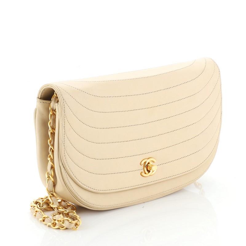 This Chanel Vintage Crescent Flap Bag Horizontal Quilted Leather Medium, crafted from neutral horizontal quilted leather, features a woven-in leather chain strap, crescent silhouette, and gold-tone hardware. Its magnetic turn-lock closure opens to a