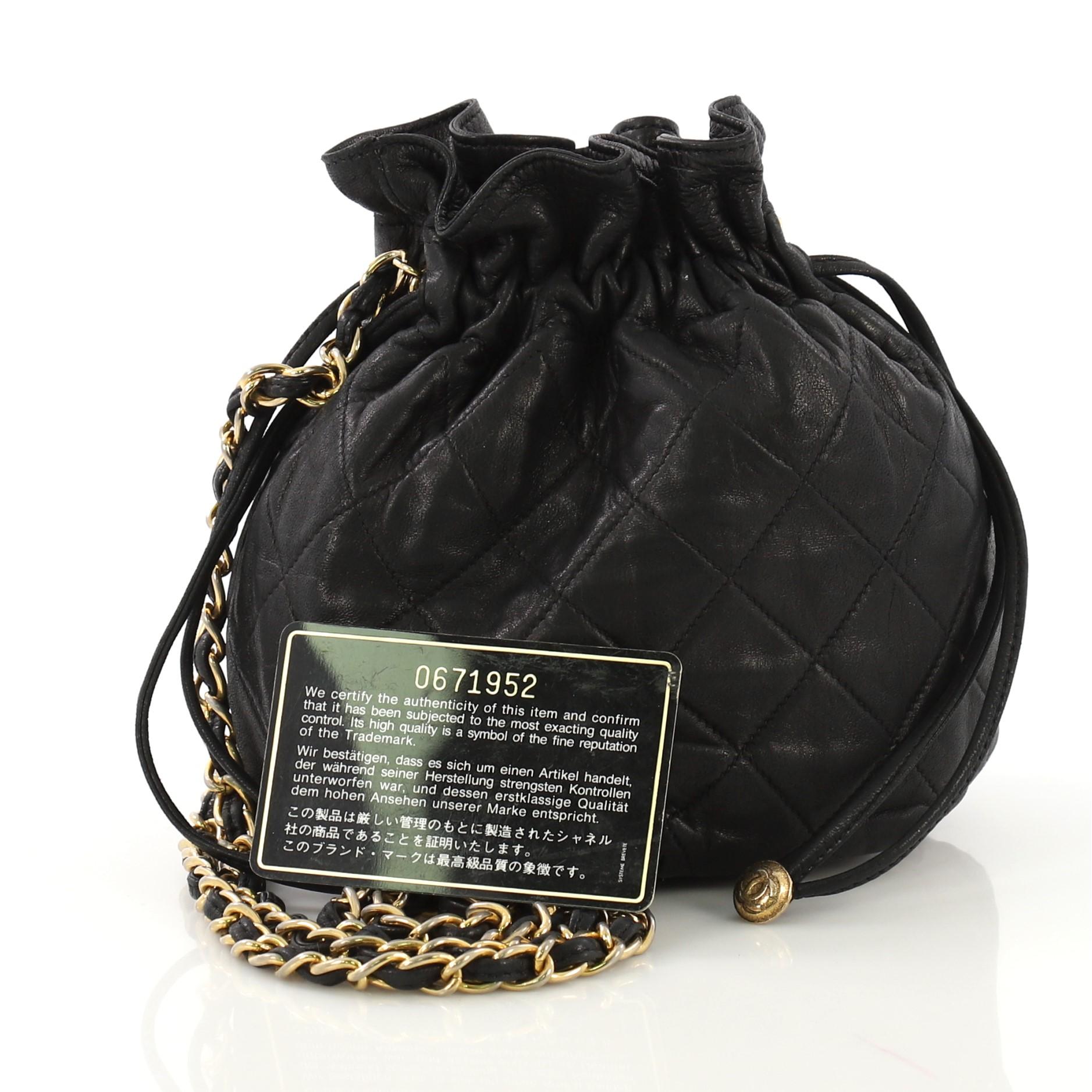This Chanel Vintage Drawstring Bucket Bag Quilted Lambskin Mini, crafted in black quilted lambskin leather, features woven-in leather chain strap and gold-tone hardware. Its drawstring closure opens to a black leather interior. Hologram sticker