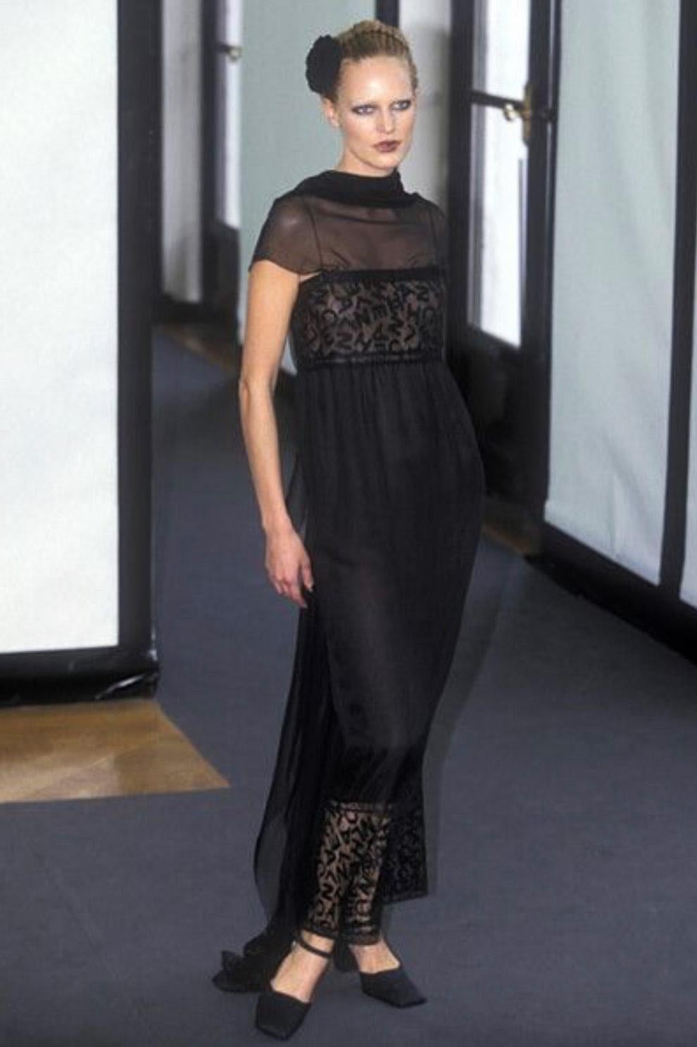 This rare Chanel evening gown is from the Fall/Winter 1998 collection, famously designed by Karl Lagerfeld. The dress is crafted from sheer black silk chiffon with a delicate lace overlay, featuring an abstract arrangement of interwoven letters
