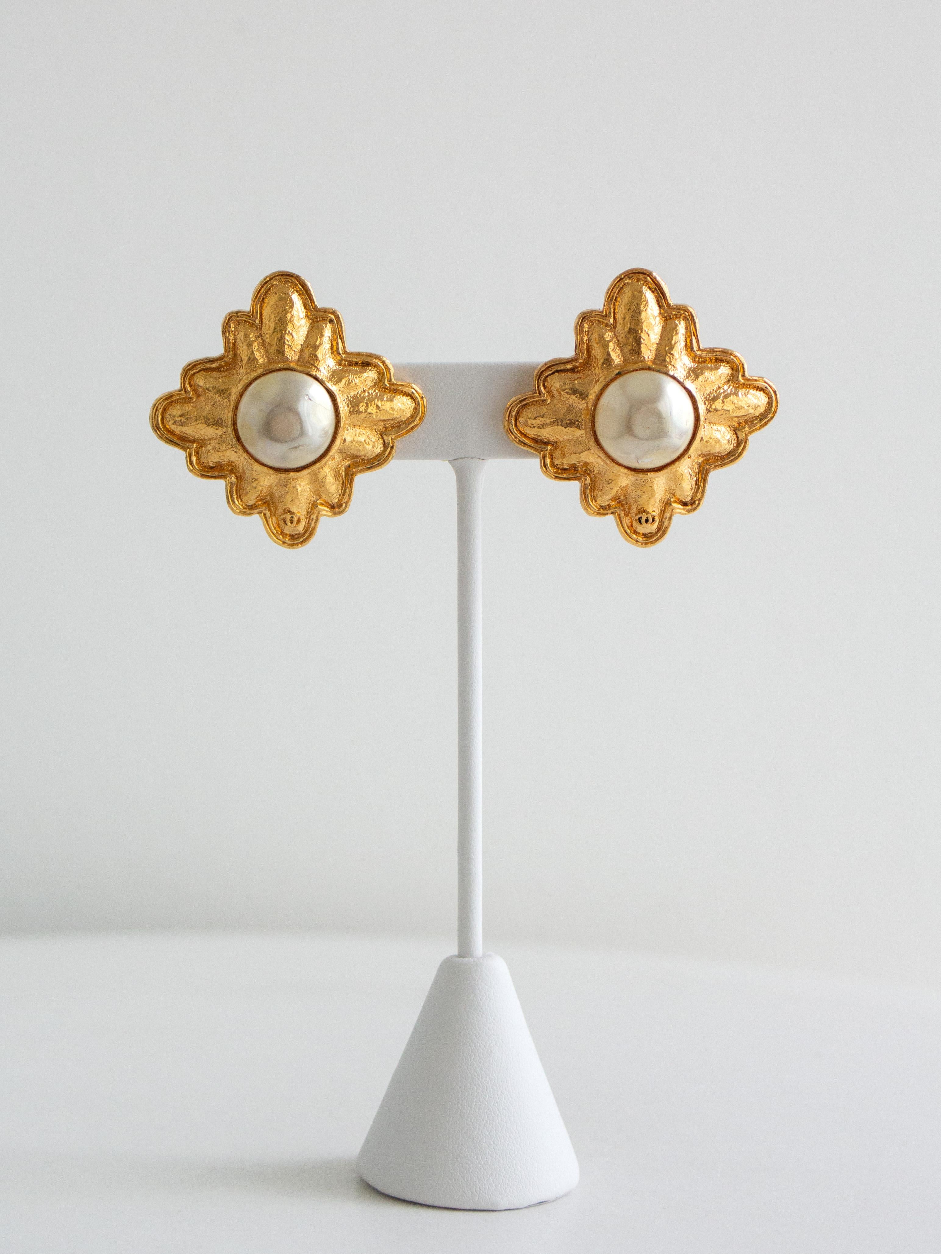 Esempio iconico della bigiotteria di Chanel dell'epoca di Lagerfeld, questi rari orecchini a clip presentano un design simmetrico a stella in placcatura d'oro fortemente strutturata, centrato da una perla finta a cupola nello stile della Maison