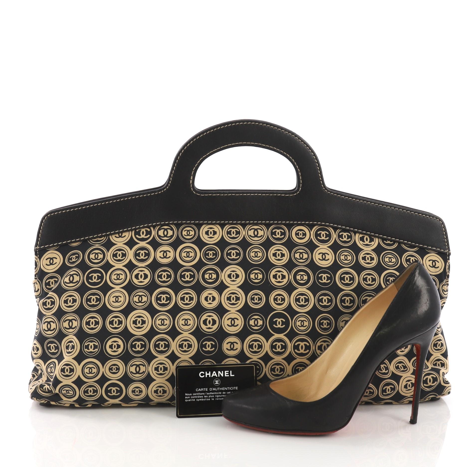 This Chanel Vintage Frame Handle Bag Printed Canvas Large, crafted from black printed canvas, features a frame top with dual cut out handles and gold-tone hardware. Its magnetic snap button closures opens to a navy fabric interior with slip pocket.