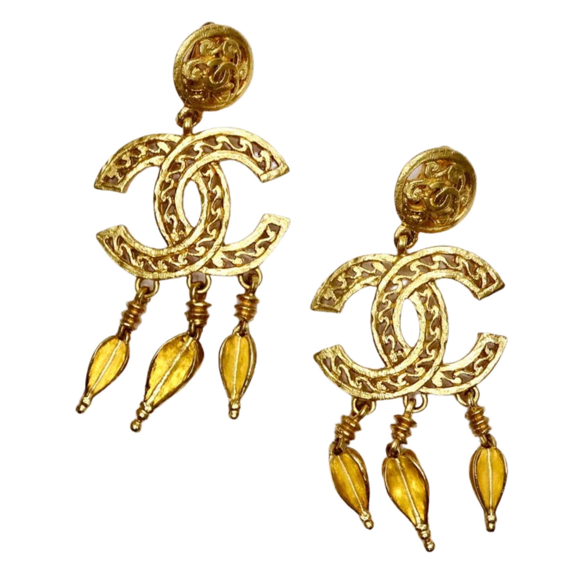 These 1990s vintage Chanel earrings are made of textured metal with an antiqued gold tone color. The earrings feature ornate cut out details, large textured CC pendants, three hanging charms, and a clip on backing. These earrings will create a lot