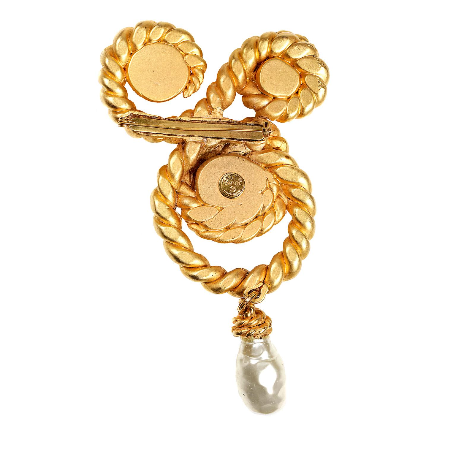 This authentic Chanel Gold Swirling Rope and Pearl Pin is in mint vintage condition from the 1970’s.  Three faux pearls are surrounded by gold tone swirling rope design.  A single teardrop pearl dangles from the bottom. 

4” at the widest point