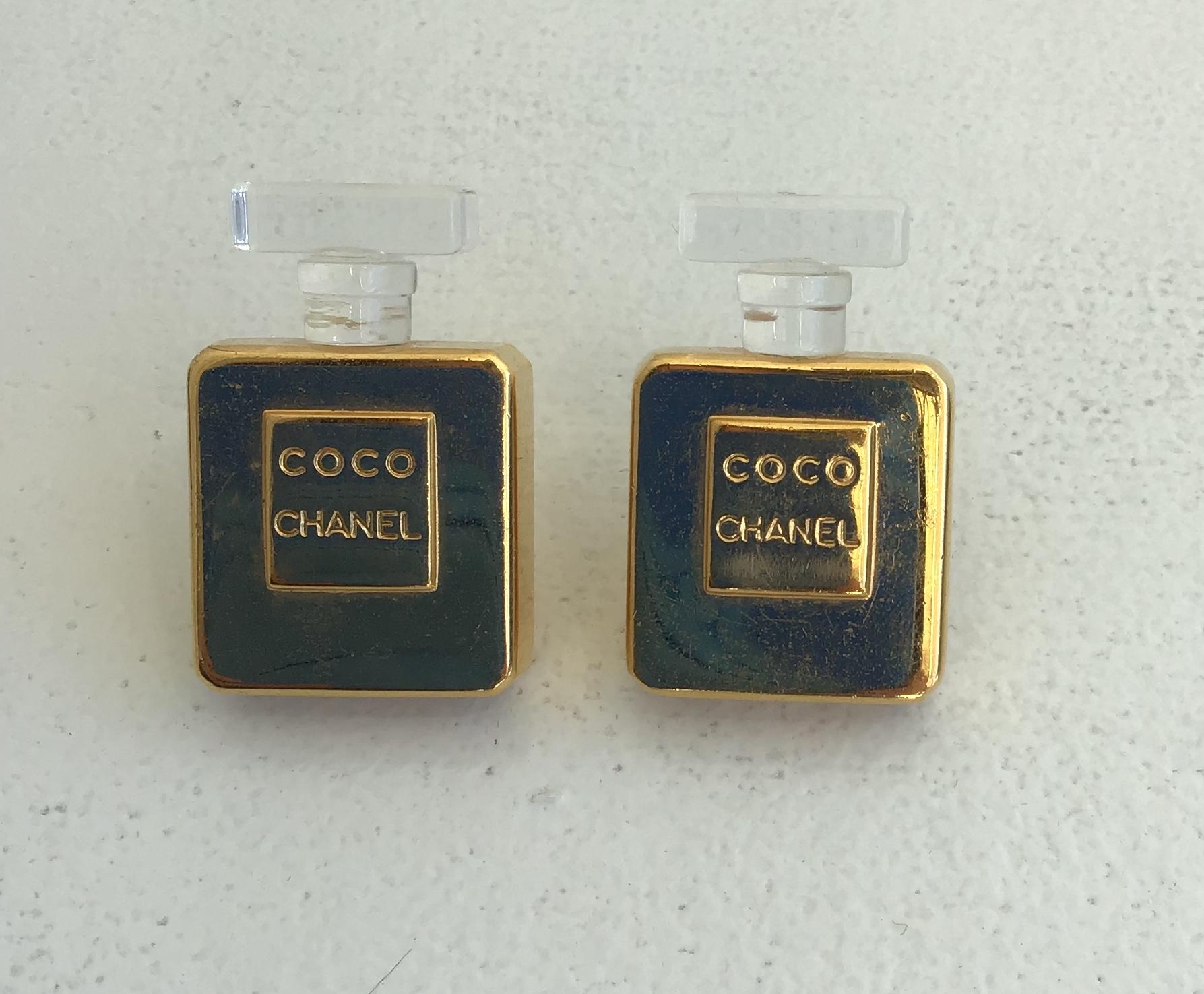 Chanel Vintage Gold Toned Coco Perfume Bottle Clip-On Earrings. Featuring a gold toned body part with clear acrylic cap detailing. Embossed Coco Chanel on the front.