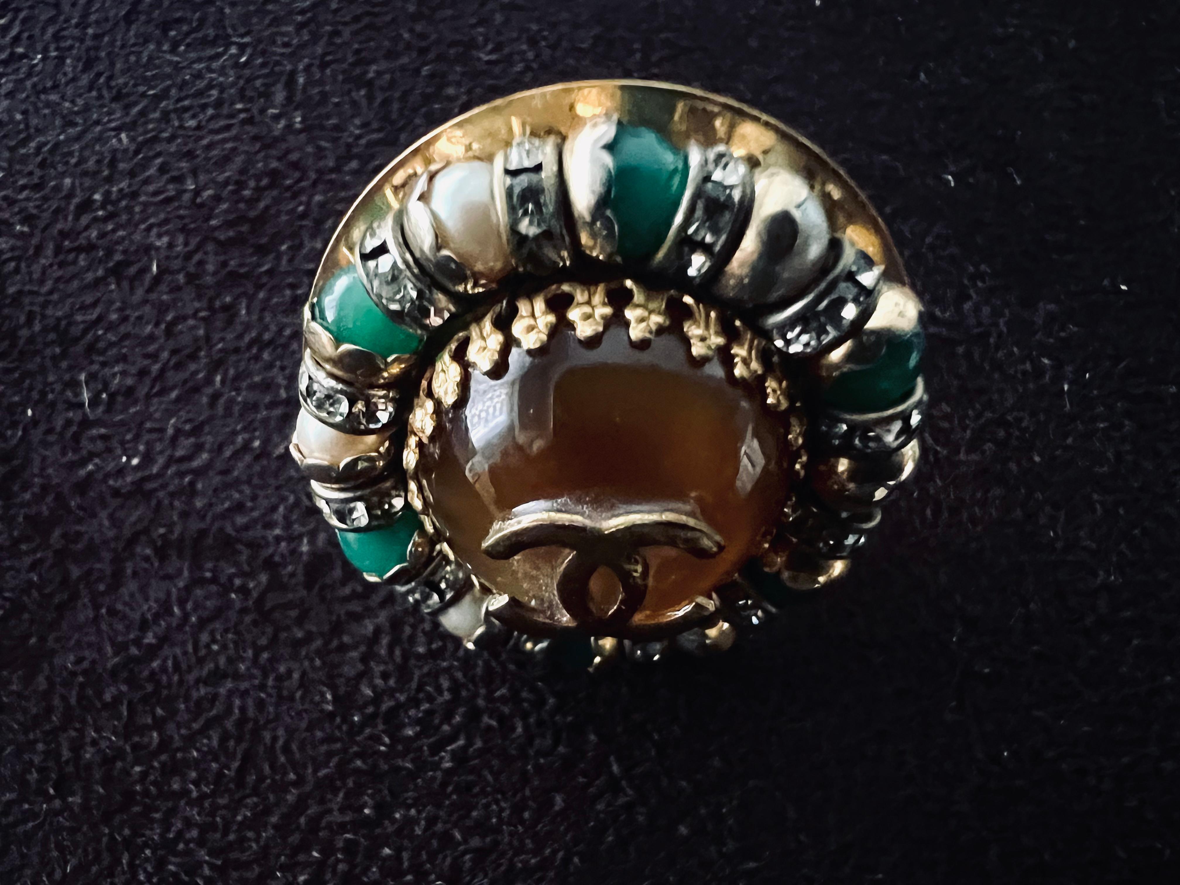 Old vintage chanel earring, circa 1970’s to 80’s. Dates unstated, “CHANEL” 
Gold Chanel logo on top of tiger eye like marbled color stone, surrounded rhinestones,green stone,pearls.