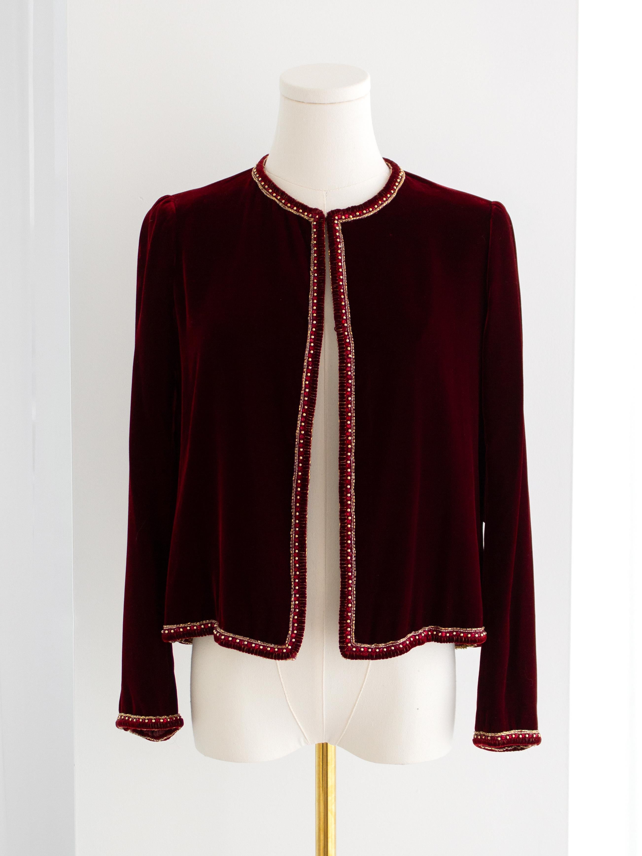 Trasportati in un passato sfarzoso con questa straordinaria giacca vintage di alta moda Chanel, risalente alla fine degli anni Settanta. Questa classica giacca senza collo dal taglio squadrato, realizzata in lussuoso velluto rosso bordeaux e