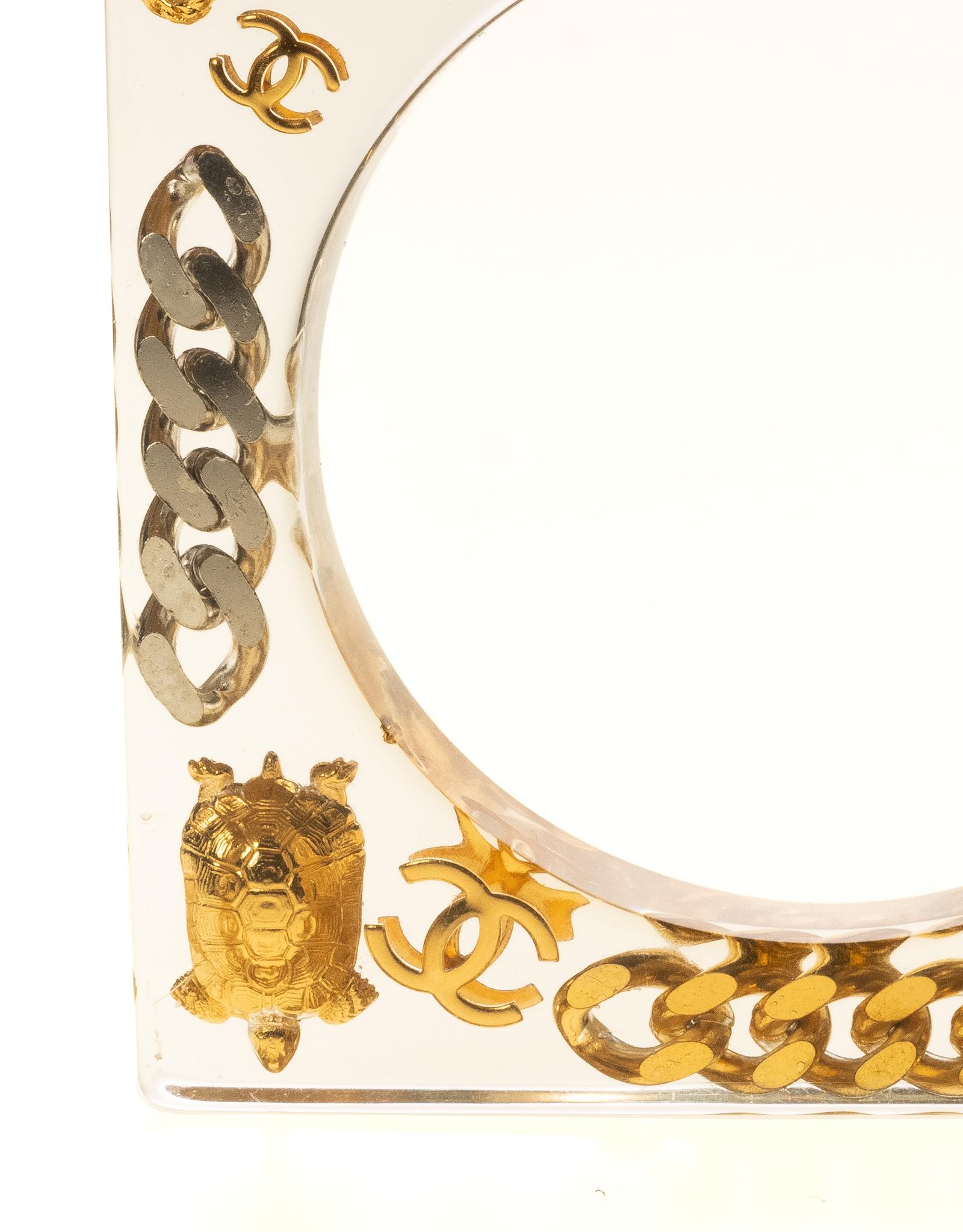 Le bracelet est composé de matériaux en plexi lucite et d'éléments en or et en argent, avec de nombreuses breloques emblématiques intégrées au bracelet. Les breloques incorporées sont les lettres CHANEL, le flacon de parfum, le n°5, la chaîne, la