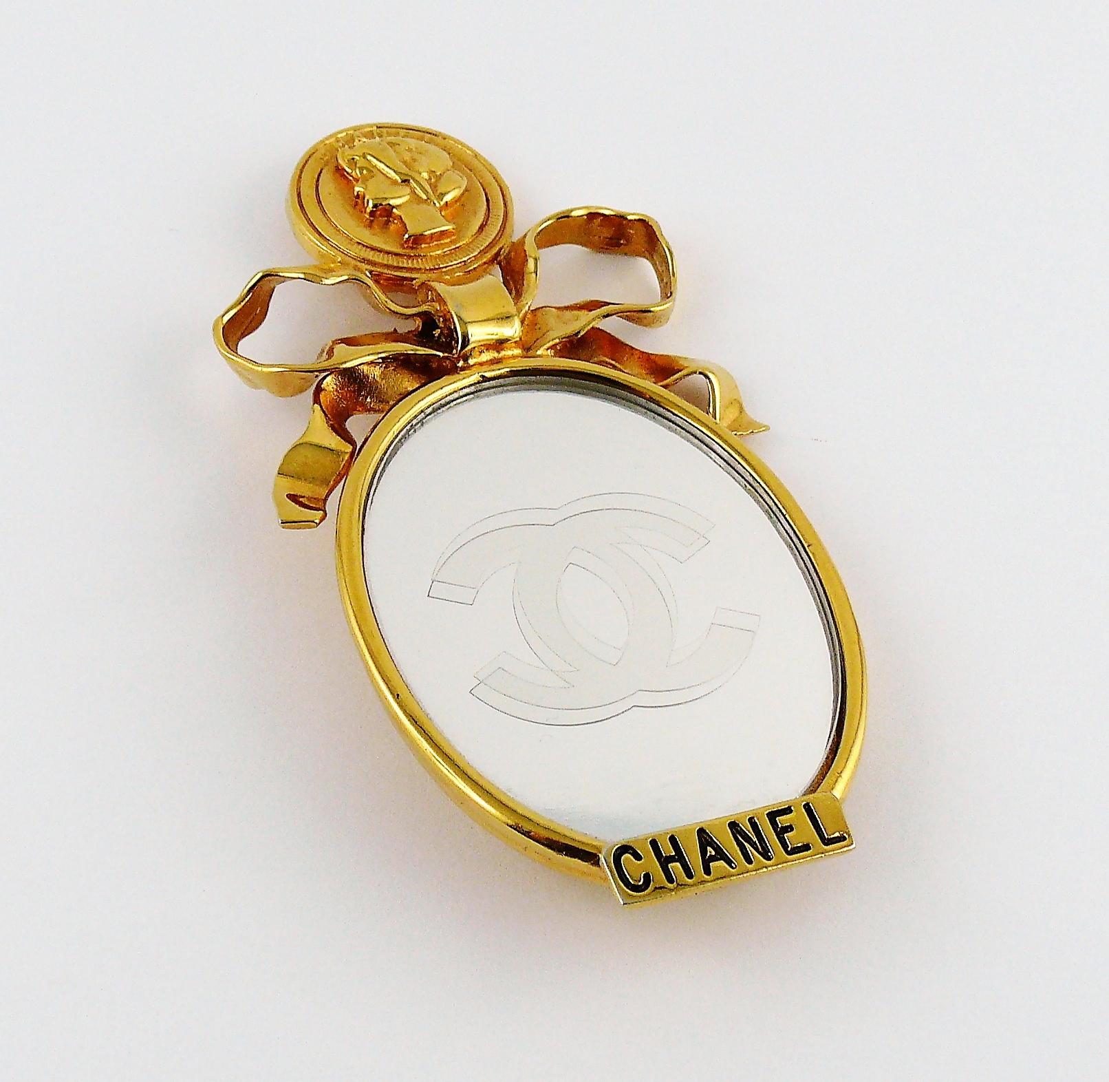 CHANEL vintage rare massive gold toned brooch featuring Mademoiselle figure at the top accentuated with a big bow, oval mirror with frosted CC logo at the center, embossed CHANEL in black at the bottom.

Embossed CHANEL on the reverse