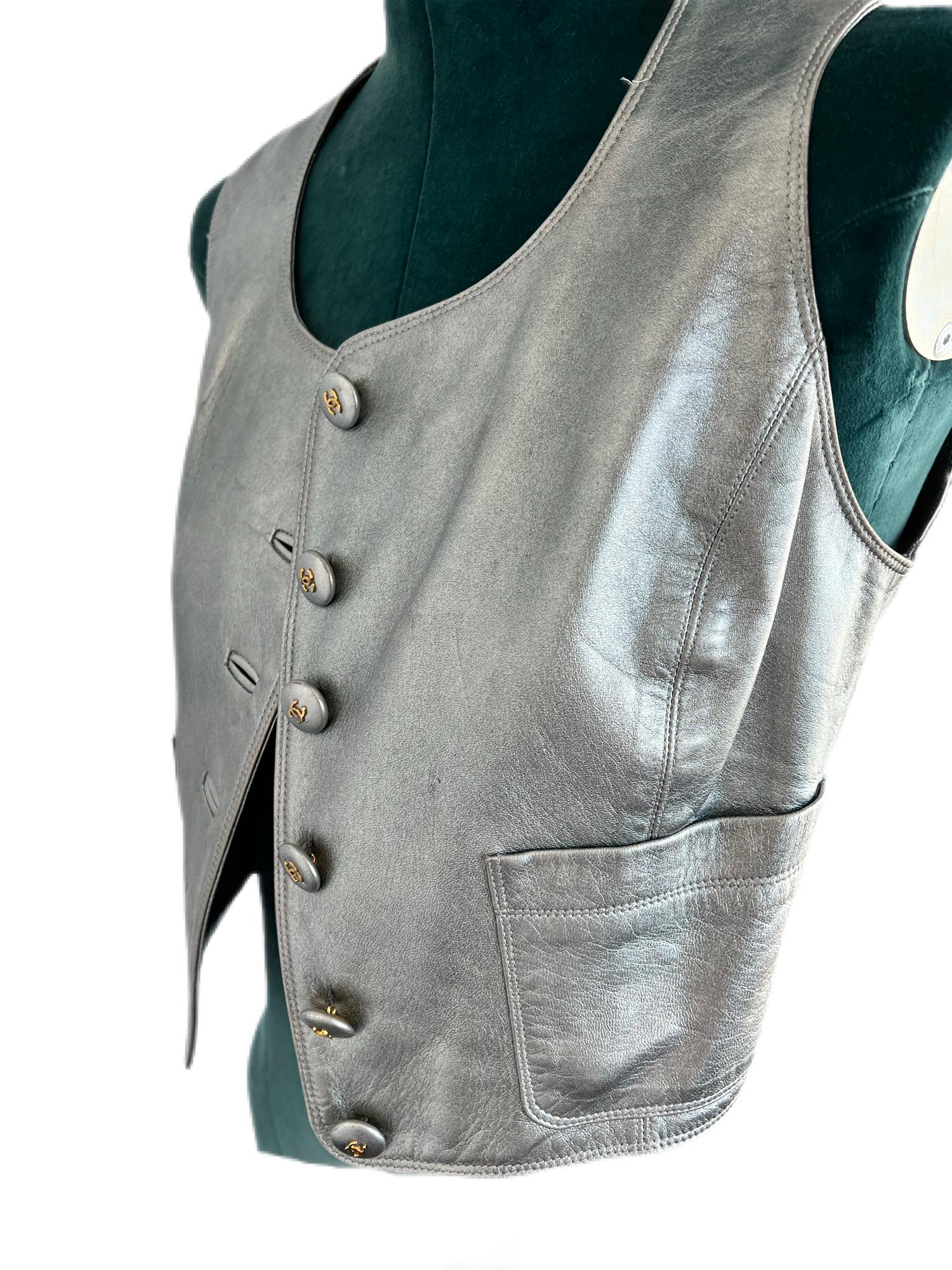This vintage Chanel vest is made from high-quality silver metallic leather and features a fitted design, CC logo button, and two front pockets. Perfect for adding a touch of luxury to any outfit.
