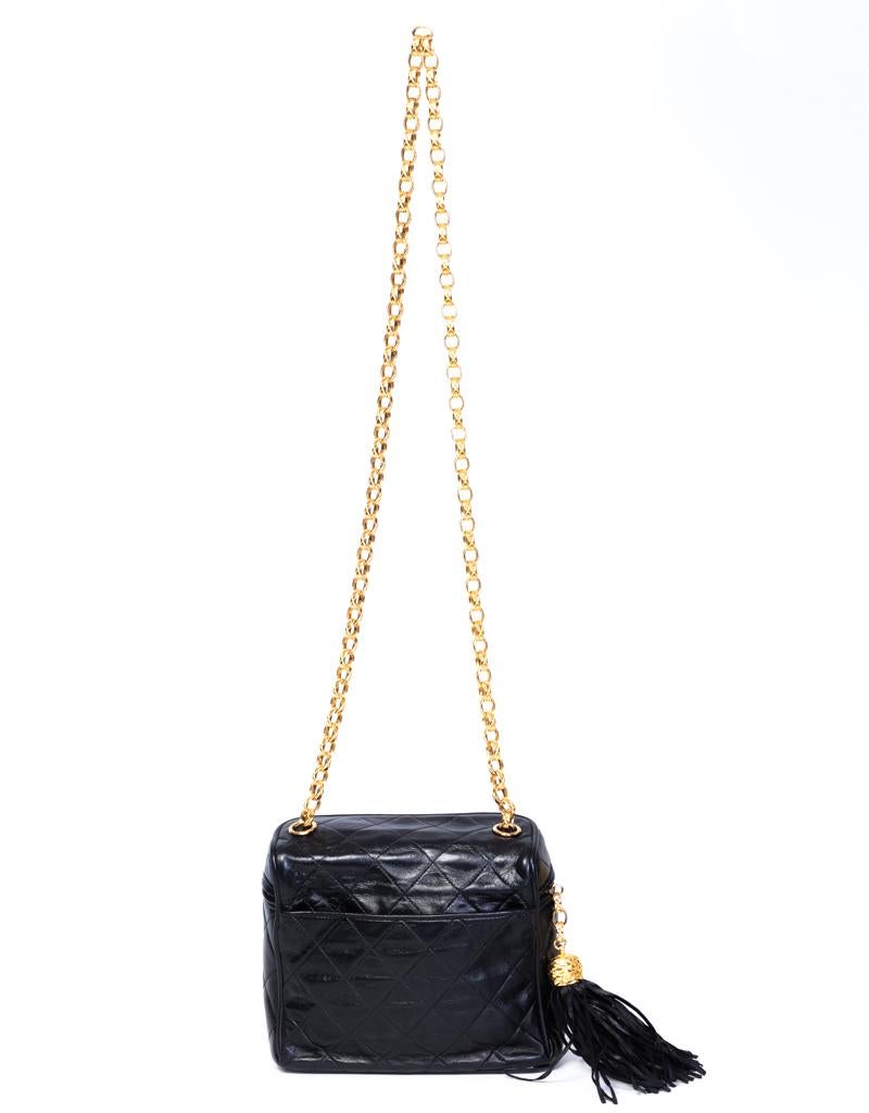 Ce mini vanity vintage de Chanel est fabriqué en cuir matelassé noir avec des éléments de quincaillerie dorés, une fermeture à glissière avec un pompon, et une sangle en chaîne dorée. L'intérieur est doublé d'un tissu crème et comporte une poche à
