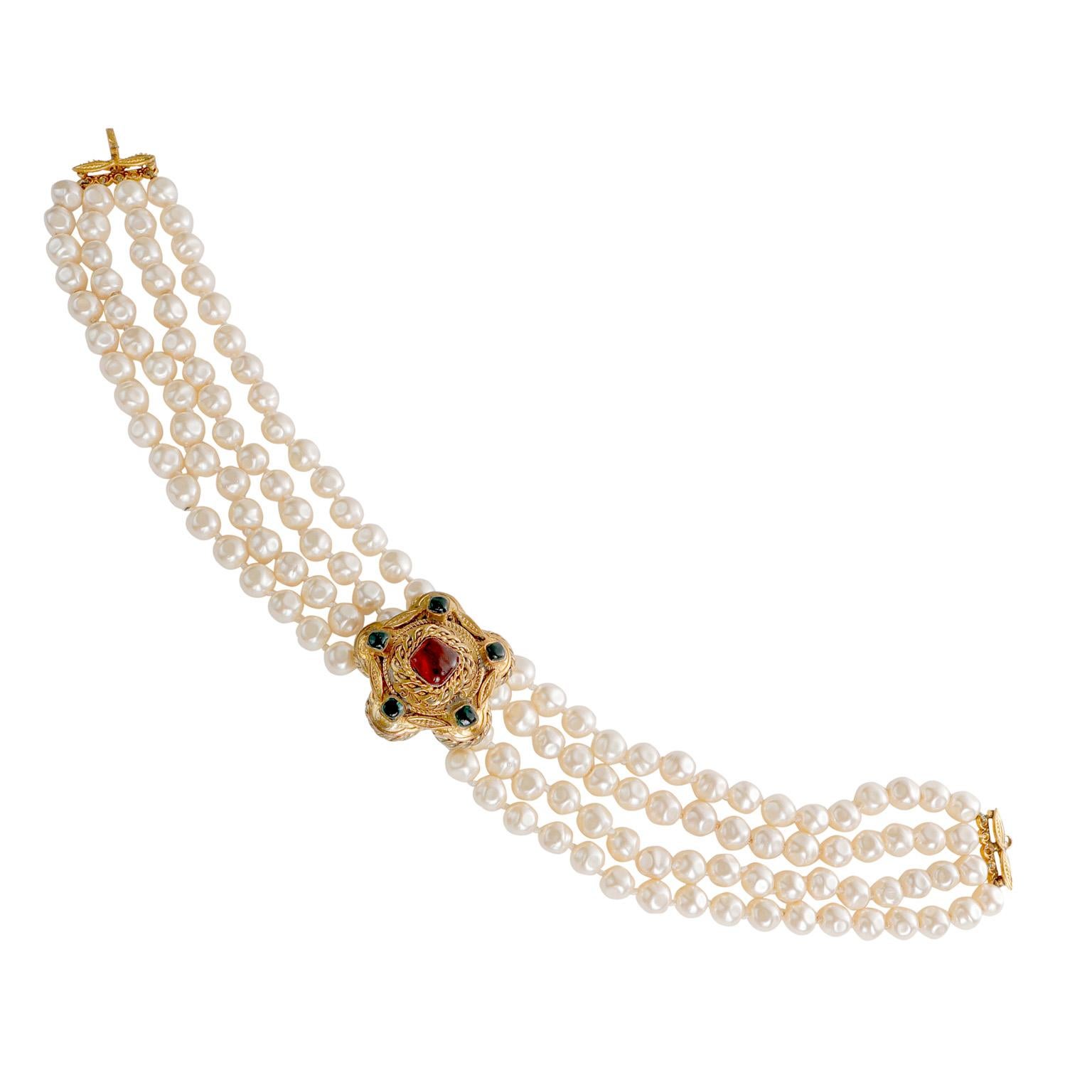 This authentic Chanel Pearl and Gripoix Choker is in excellent vintage condition.  Very early vintage four-layer faux pearl choker with gold tone ornate centerpiece.  Dark green and red Gripoix stone details.

PBF 13123