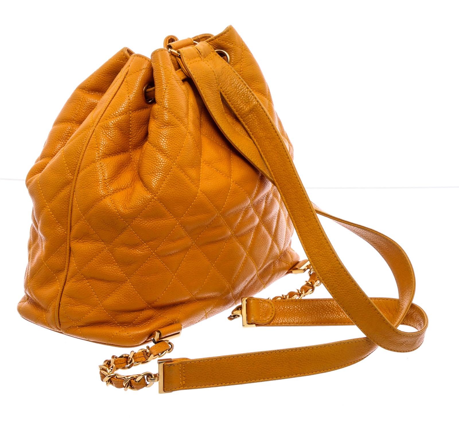 Mustard yellow quilted Caviar leather vintage Chanel drawstring backpack with gold-tone hardware, dual Caviar and chain-link shoulder straps, single chain-link and Caviar leather top handle, logo charm at side, tonal grosgrain lining, dual zip