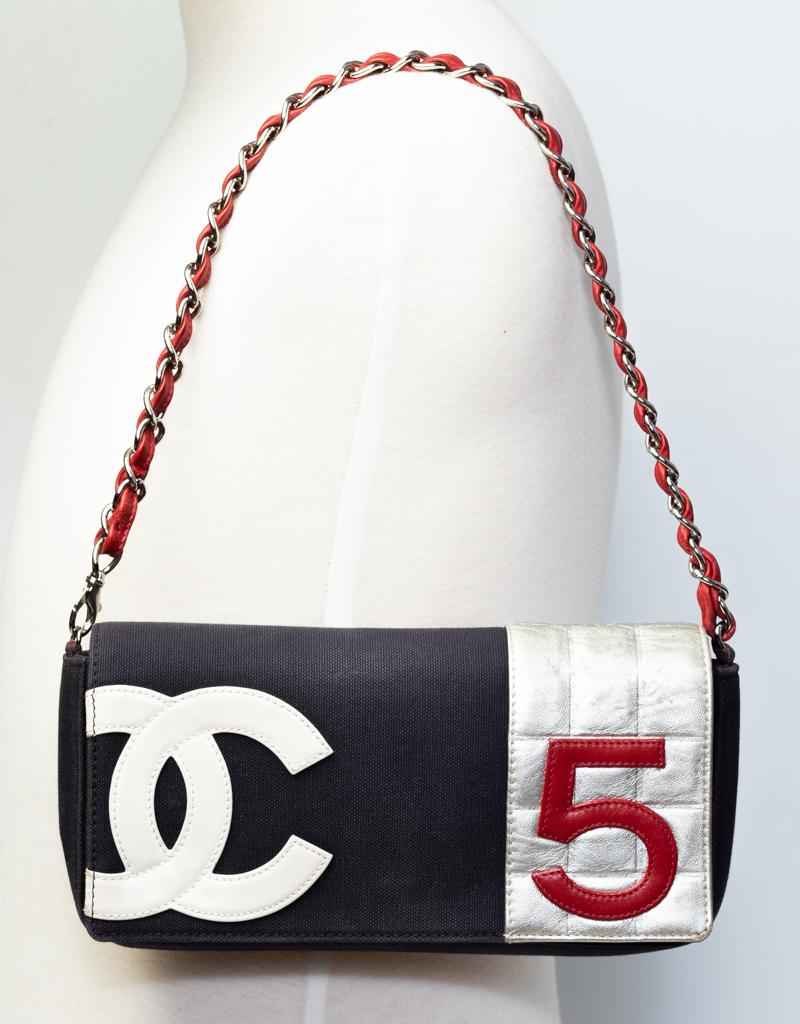 This Chanel No. 5 bag is constructed in in navy blue canvas and square quilted silver leather. Featuring a silver toned chain interlaced with red leather, a canvas exterior with 'CC' in white leather and the number '5' in red leather, and an