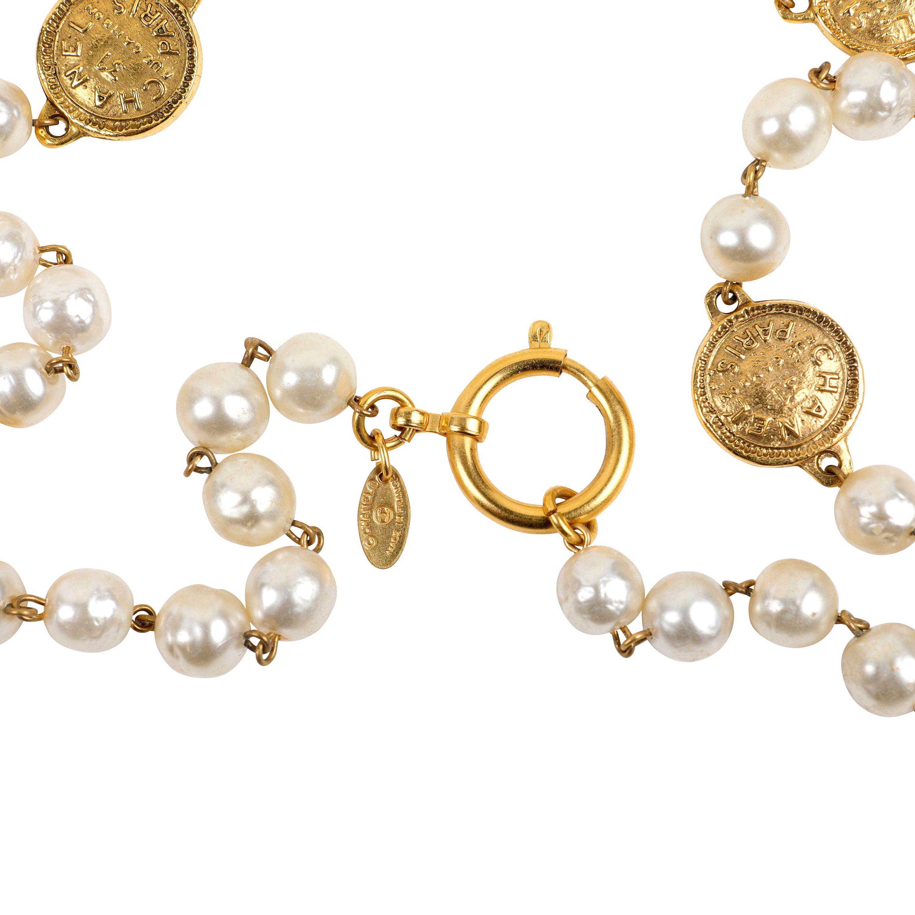 Este auténtico collar Chanel de perlas y monedas de la Rue Cambon está en excelentes condiciones vintage de los años 80.  Las perlas de imitación se entremezclan con monedas grabadas en tono dorado de 31 Rue Cambon.  Fabricado en Francia.  Bolsa o